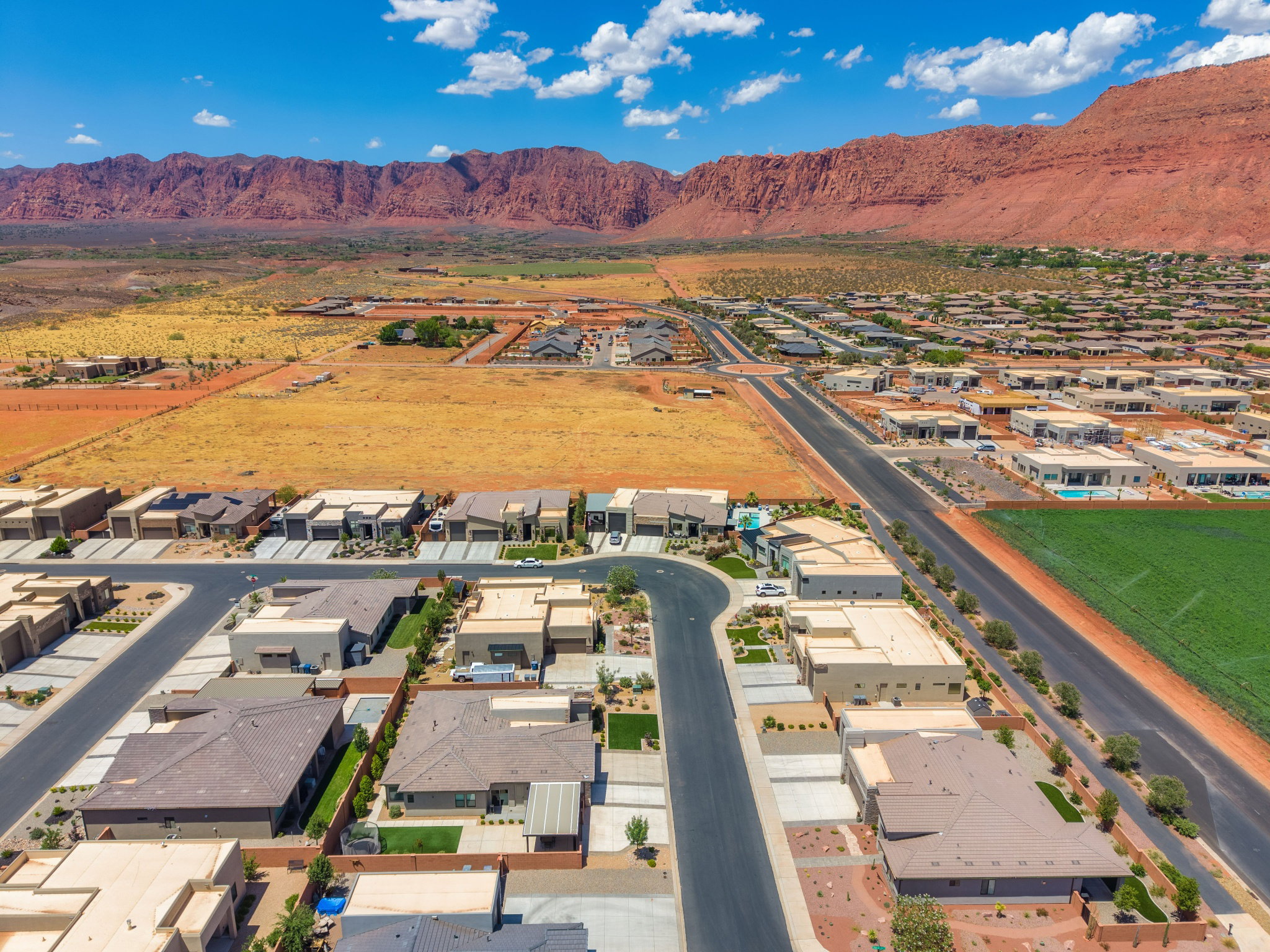 Expansive residential development with contemporary homes, paved streets, and a backdrop of red rock mountains