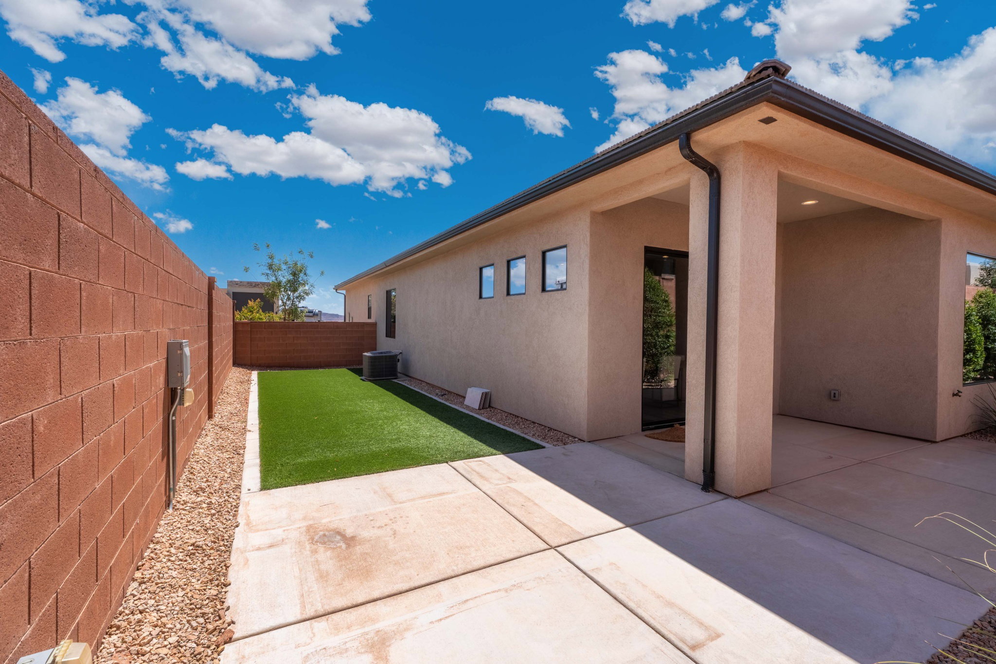 Private yard space featuring a solid block wall, low-maintenance artificial turf, a concrete patio, and a covered entry