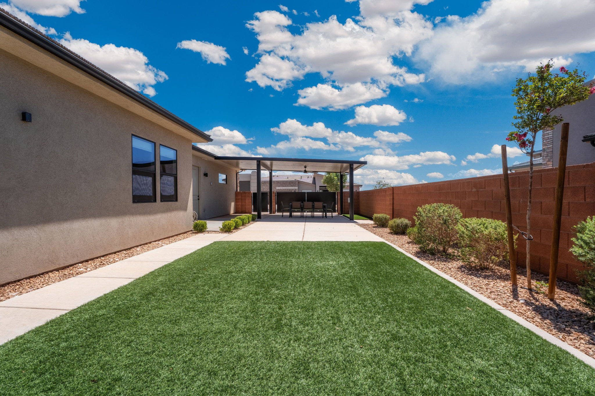 Spacious backyard featuring artificial turf, a concrete patio, a covered pergola, and a block wall perimeter