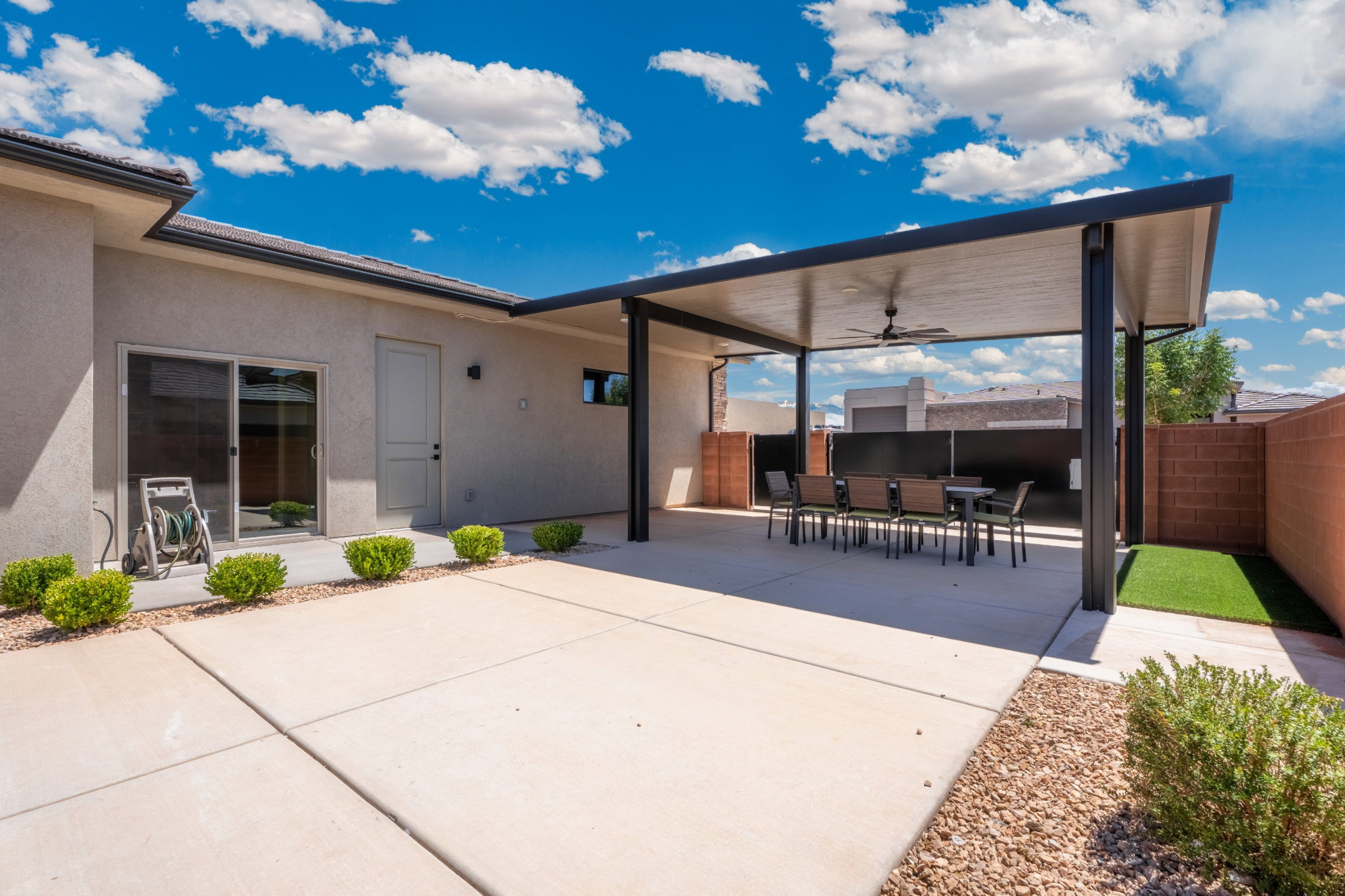 Expansive concrete patio featuring a large covered patio with a ceiling fan, a sliding glass door entry, and a dedicated artificial turf area