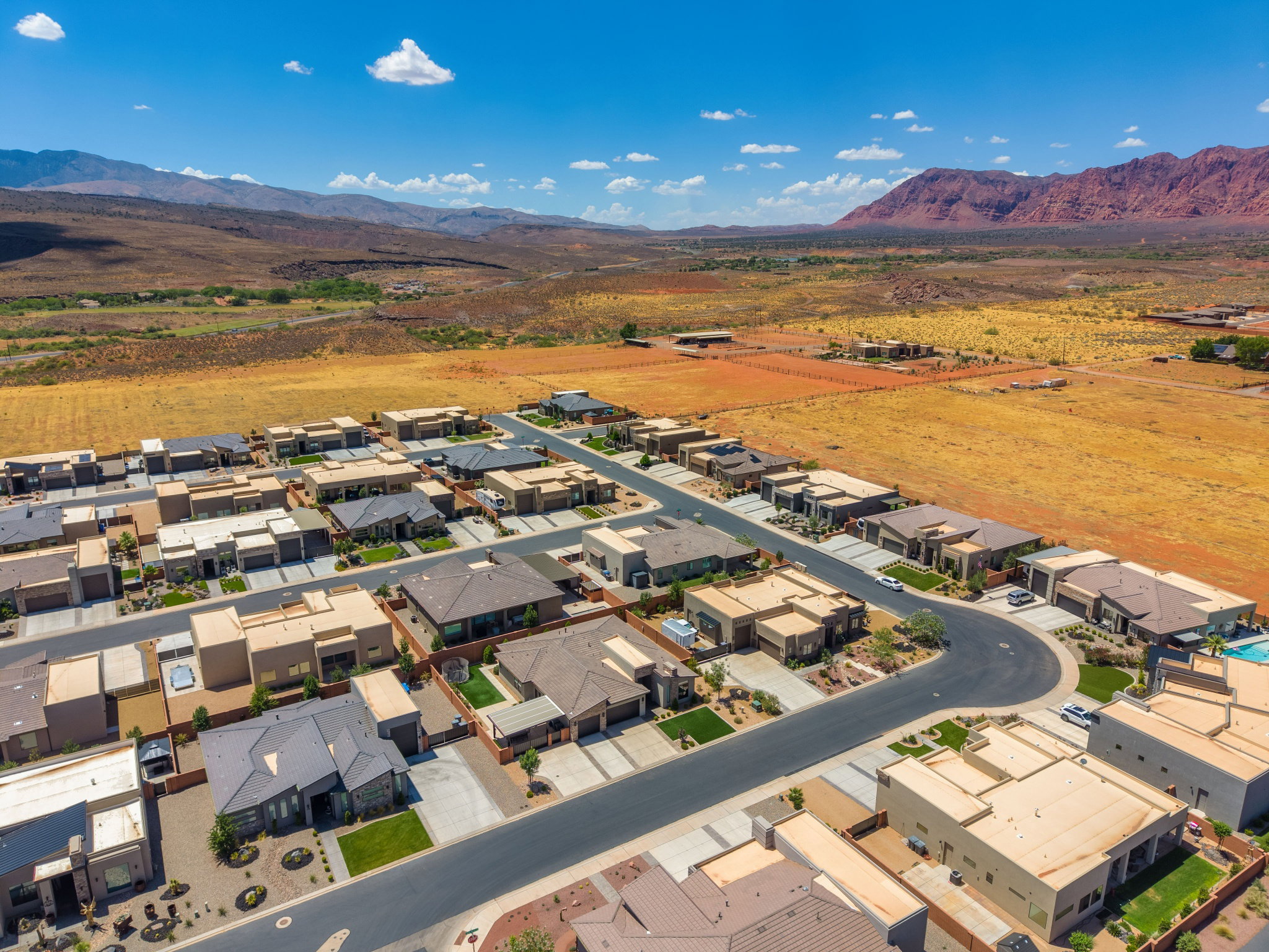 Modern residential development featuring a paved road network, uniform architectural styles, landscaped properties, and surrounding natural desert landscape with distant mountains