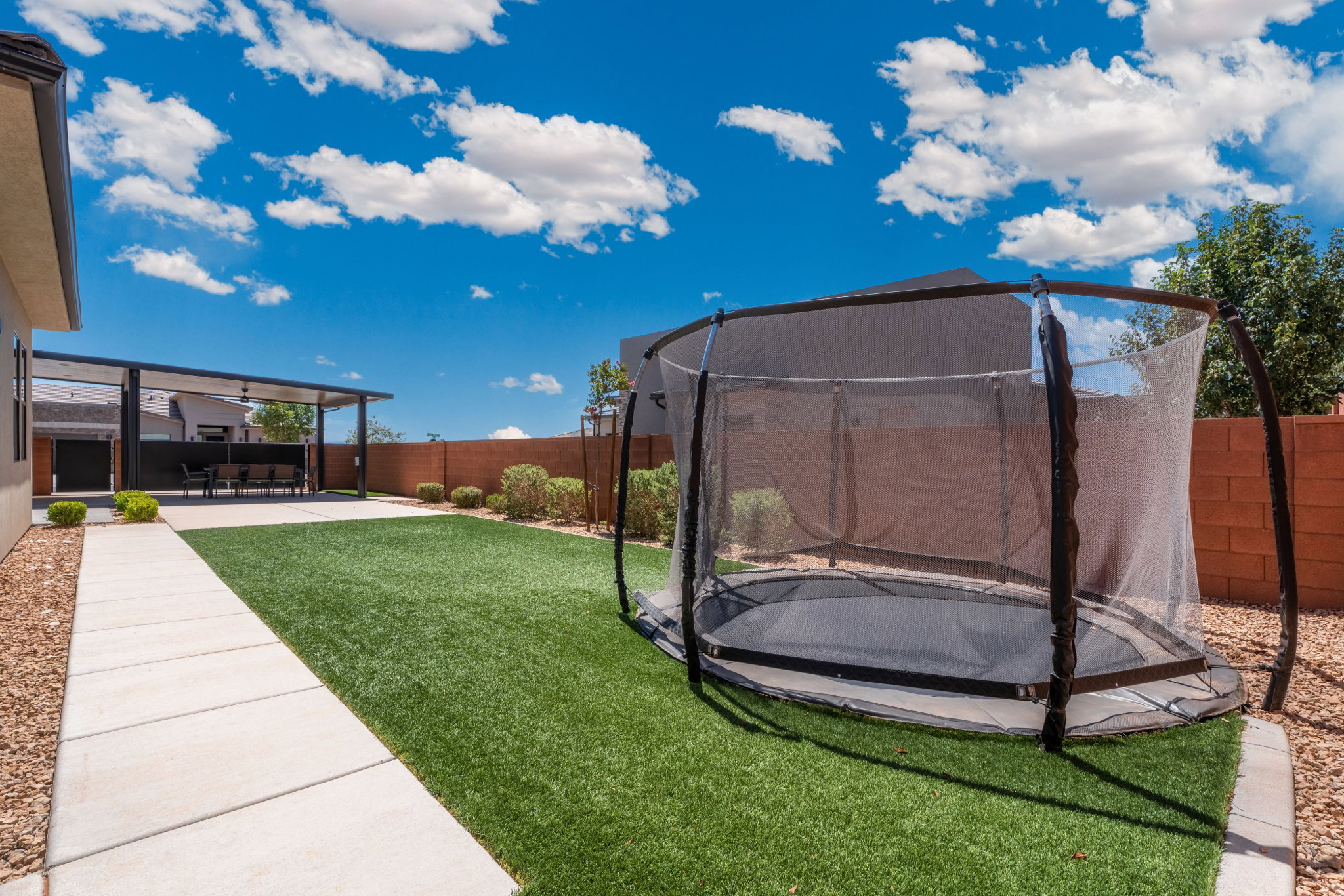 Expansive backyard featuring a covered patio, artificial turf lawn, concrete walkway, and gravel landscaping