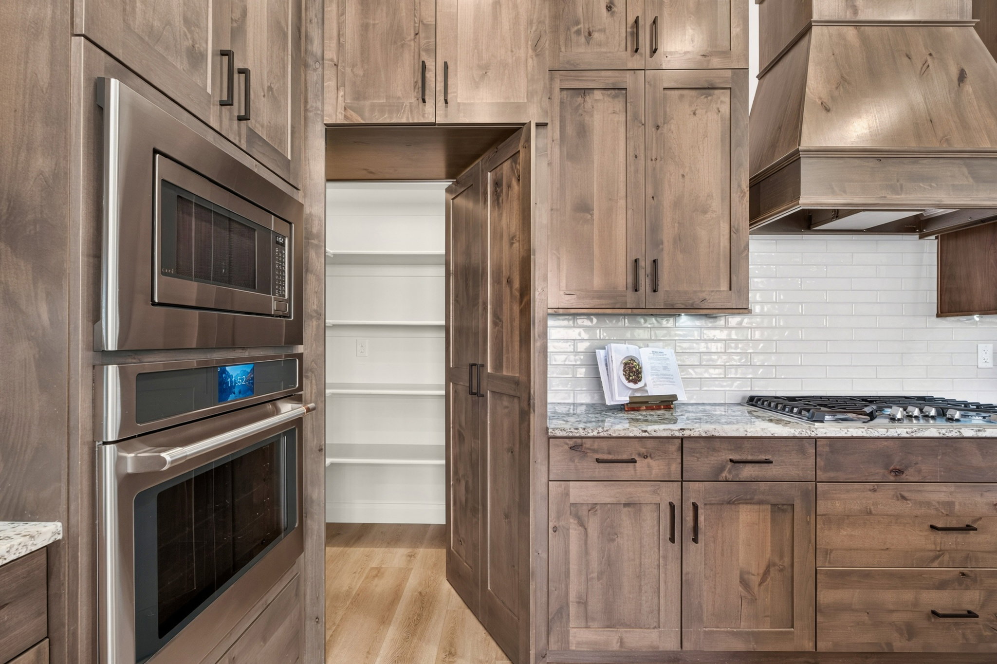 Built-in stainless steel double oven, microwave, and gas cooktop with a custom wood hood