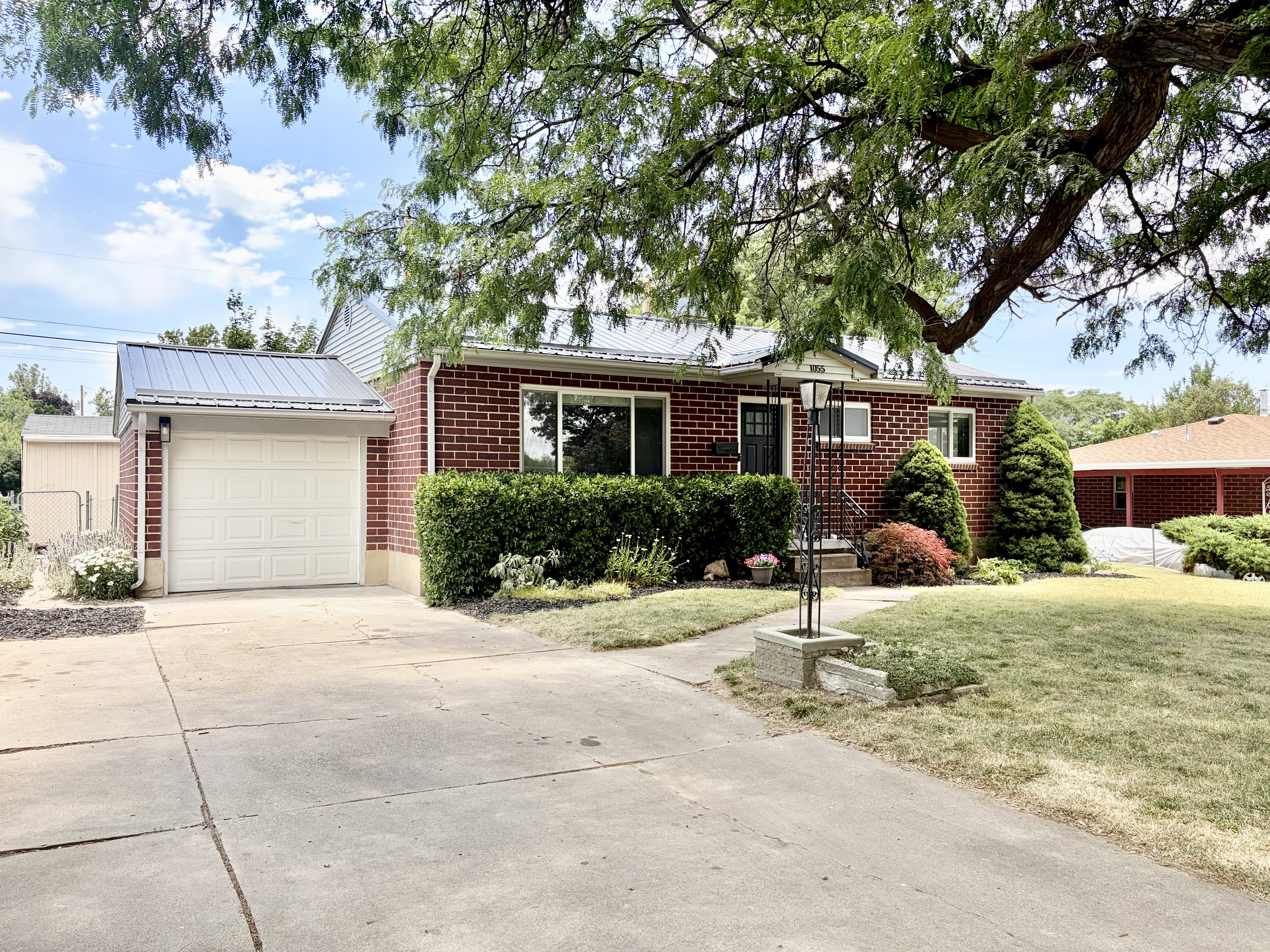 Brick facade residence featuring a covered entry, single-car garage with a panel door, and a metal roof