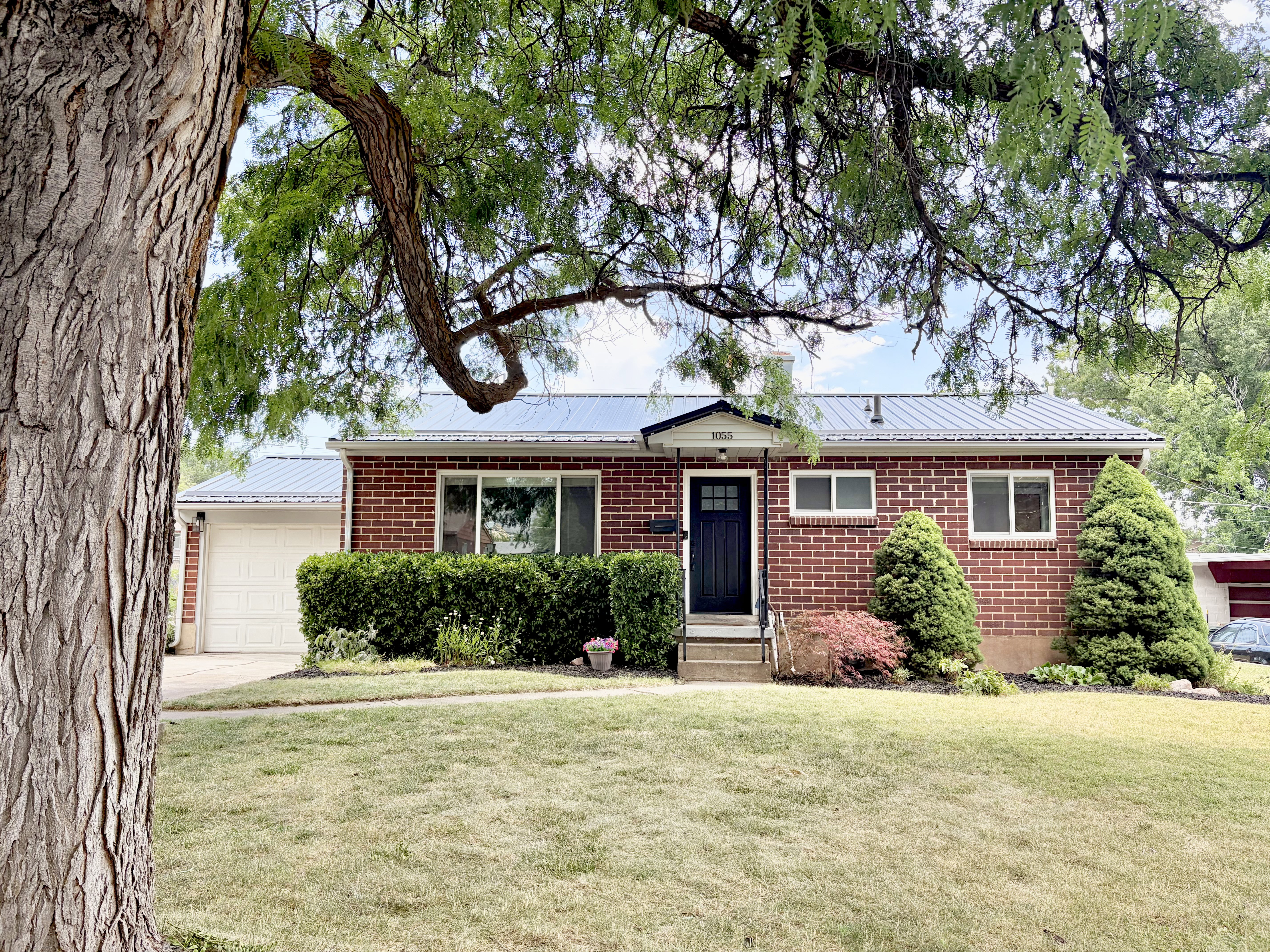 Brick exterior residence with a metal roof, featuring a single-car garage and a front entrance with a dark paneled door
