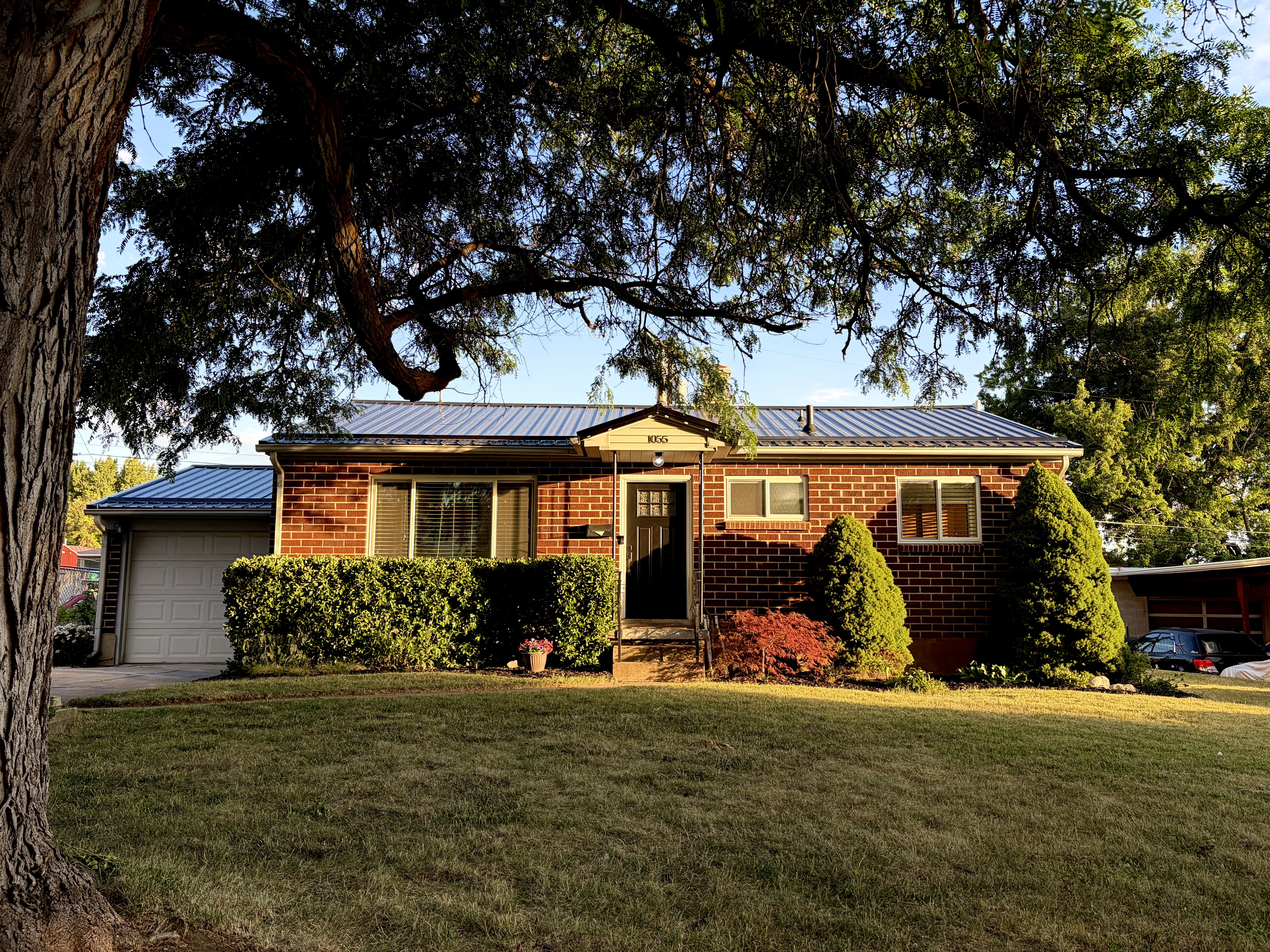 Brick exterior featuring a metal roof, attached single-car garage, and established front lawn