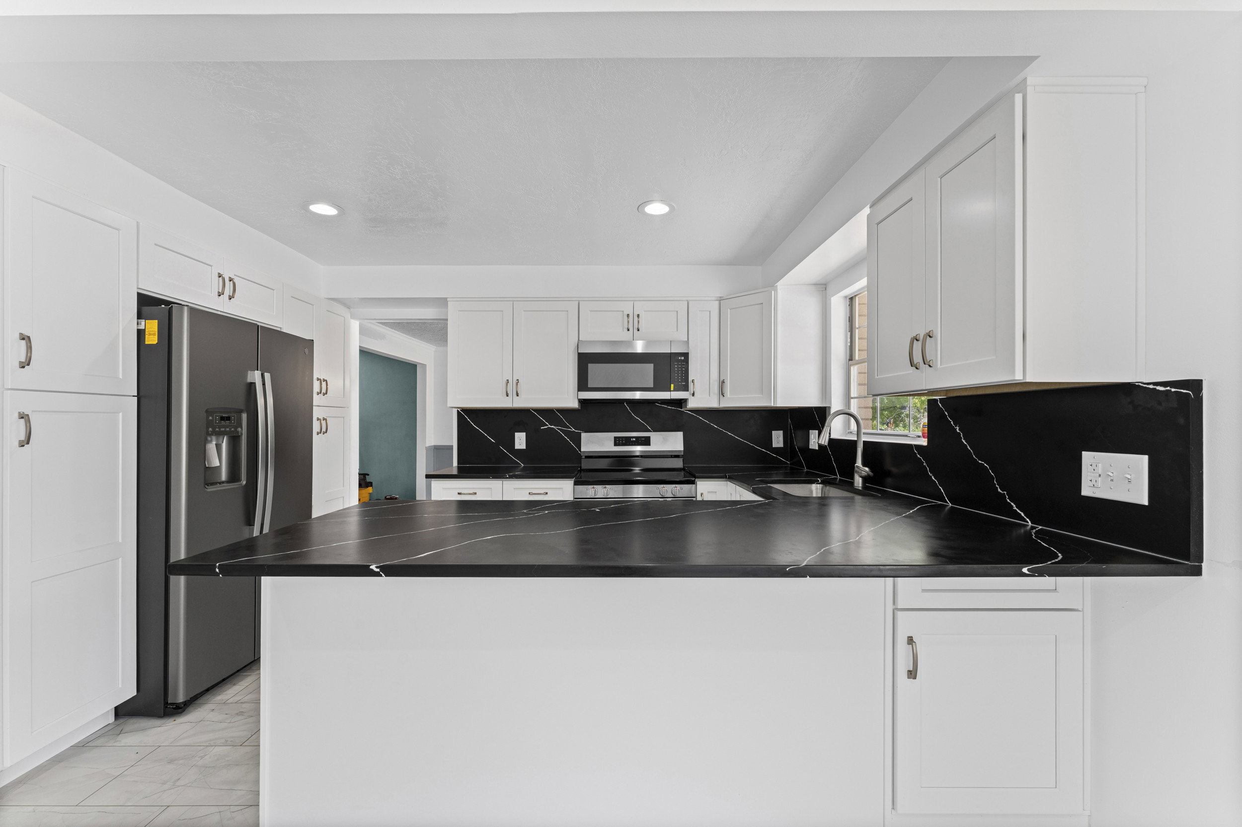 Kitchen featuring white cabinetry, dark countertops with light veining, a stainless steel refrigerator, a stainless steel microwave, and recessed lighting