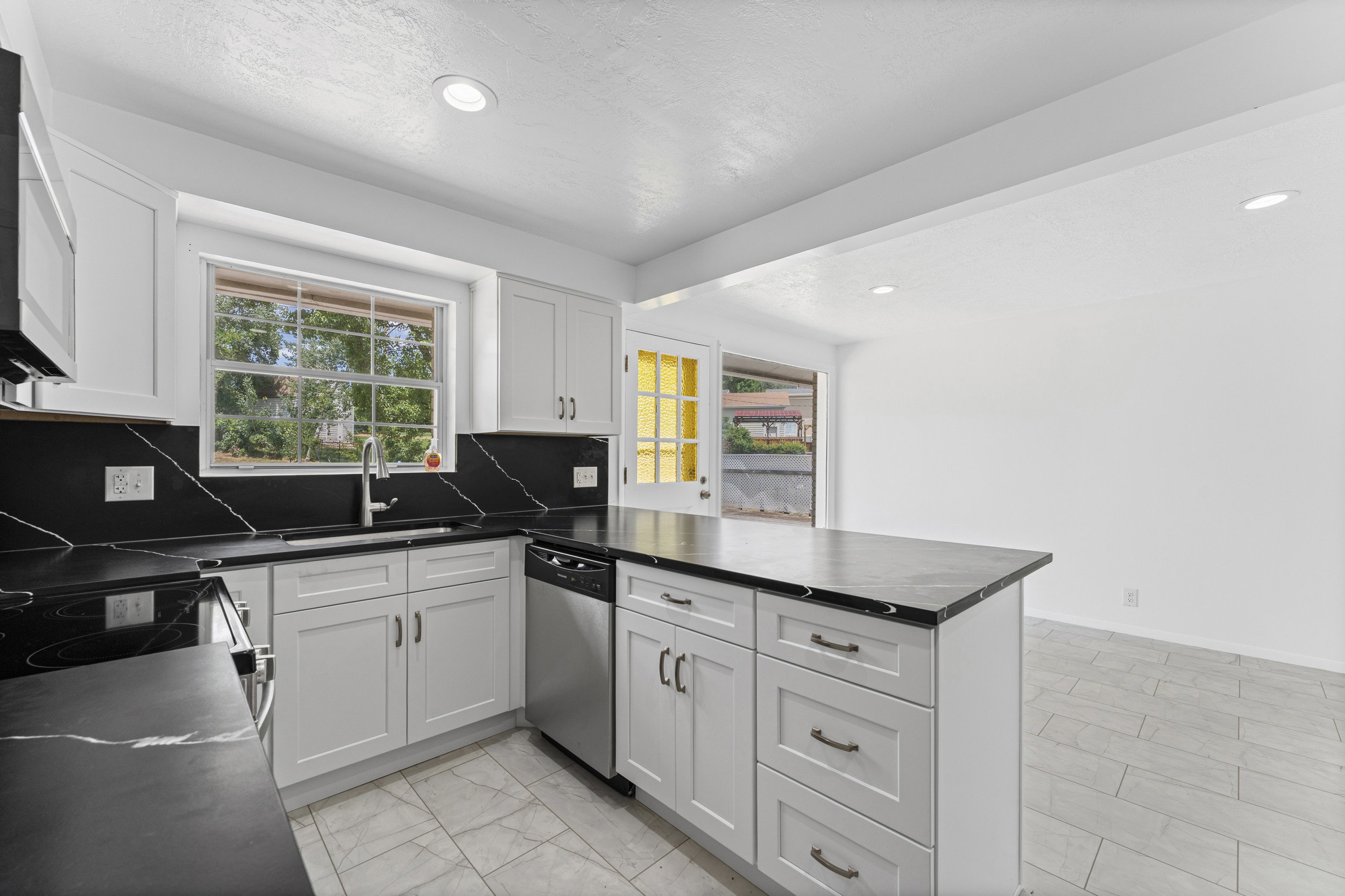 Kitchen featuring white shaker cabinetry, black countertops with white veining, stainless steel appliances, and a central island
