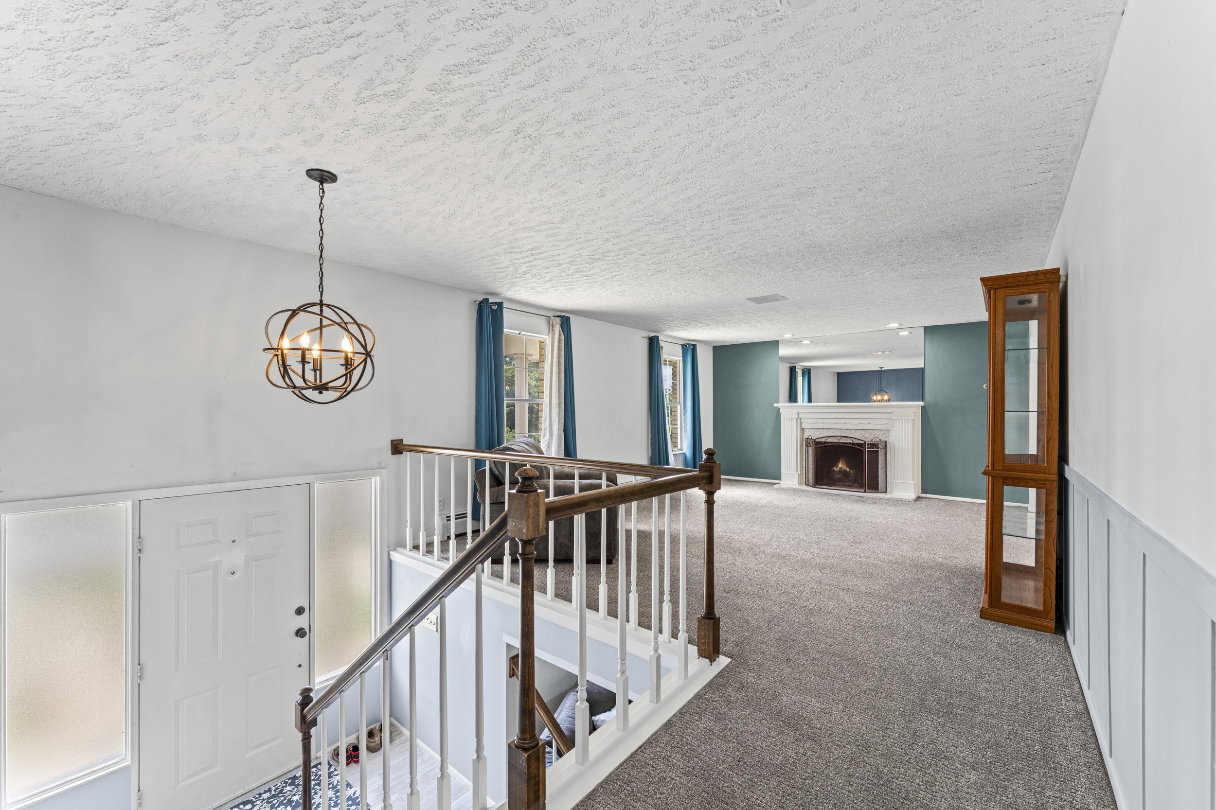 Two-story entry foyer with a decorative chandelier, white panel door with frosted sidelights, and carpeted flooring