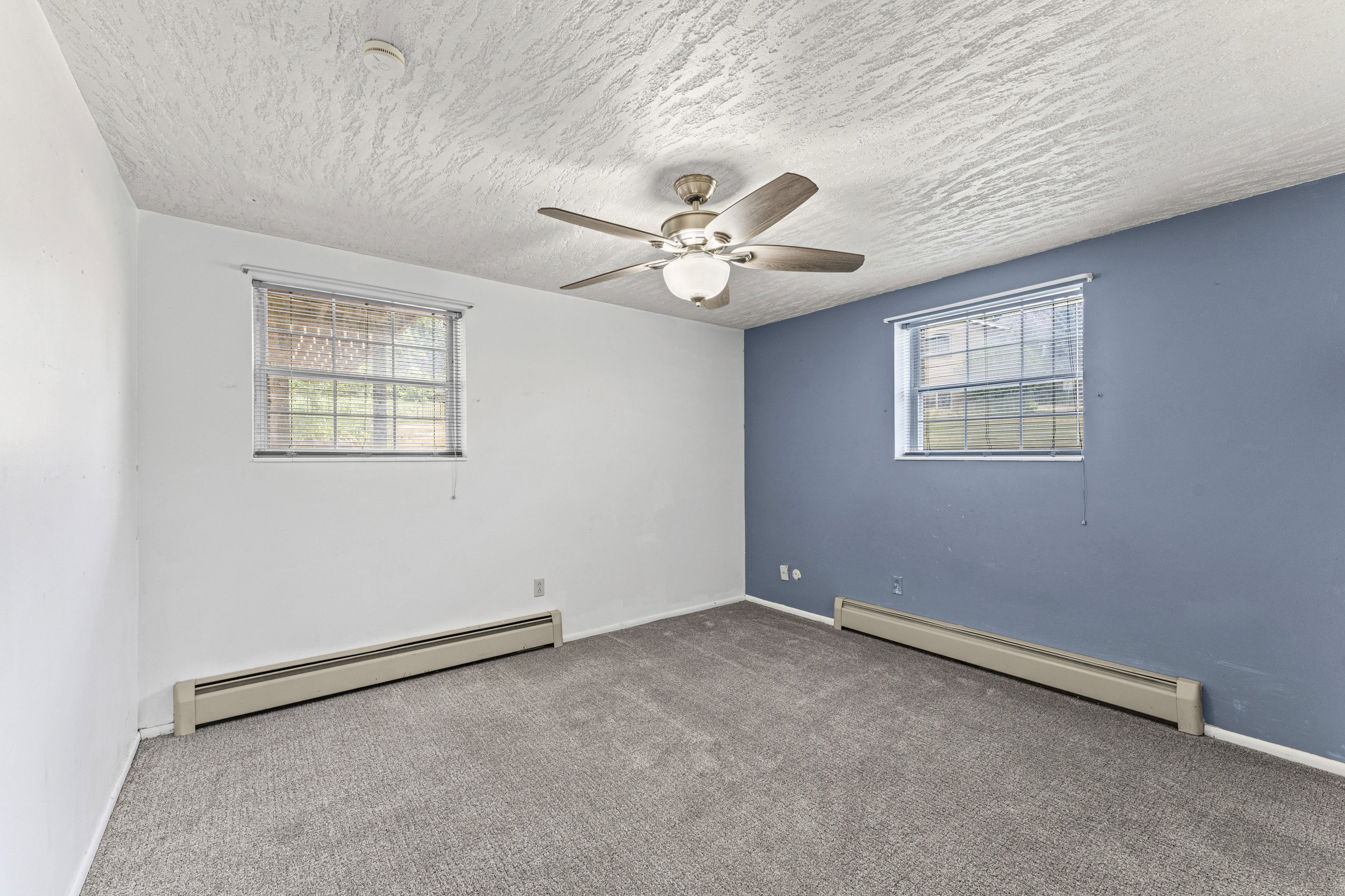 Room with gray textured carpeting, a ceiling fan with integrated lighting, and two windows with blinds