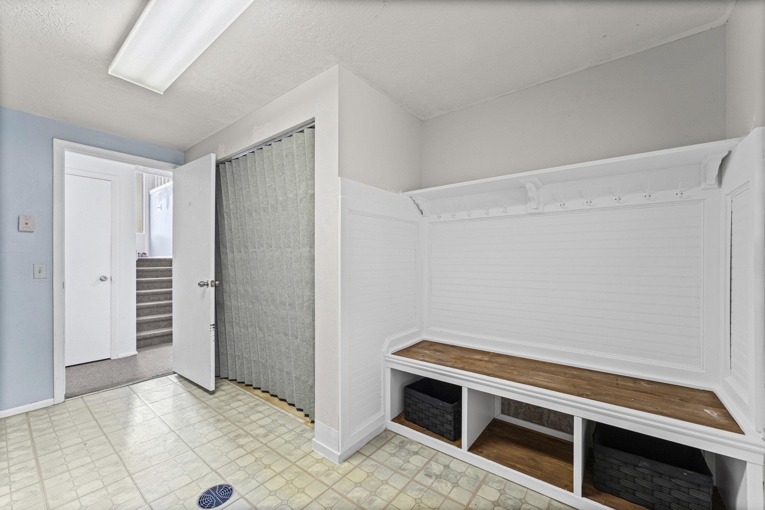 Built-in storage bench with wood-finish top and lower cubbies, beadboard backing, and coat hooks