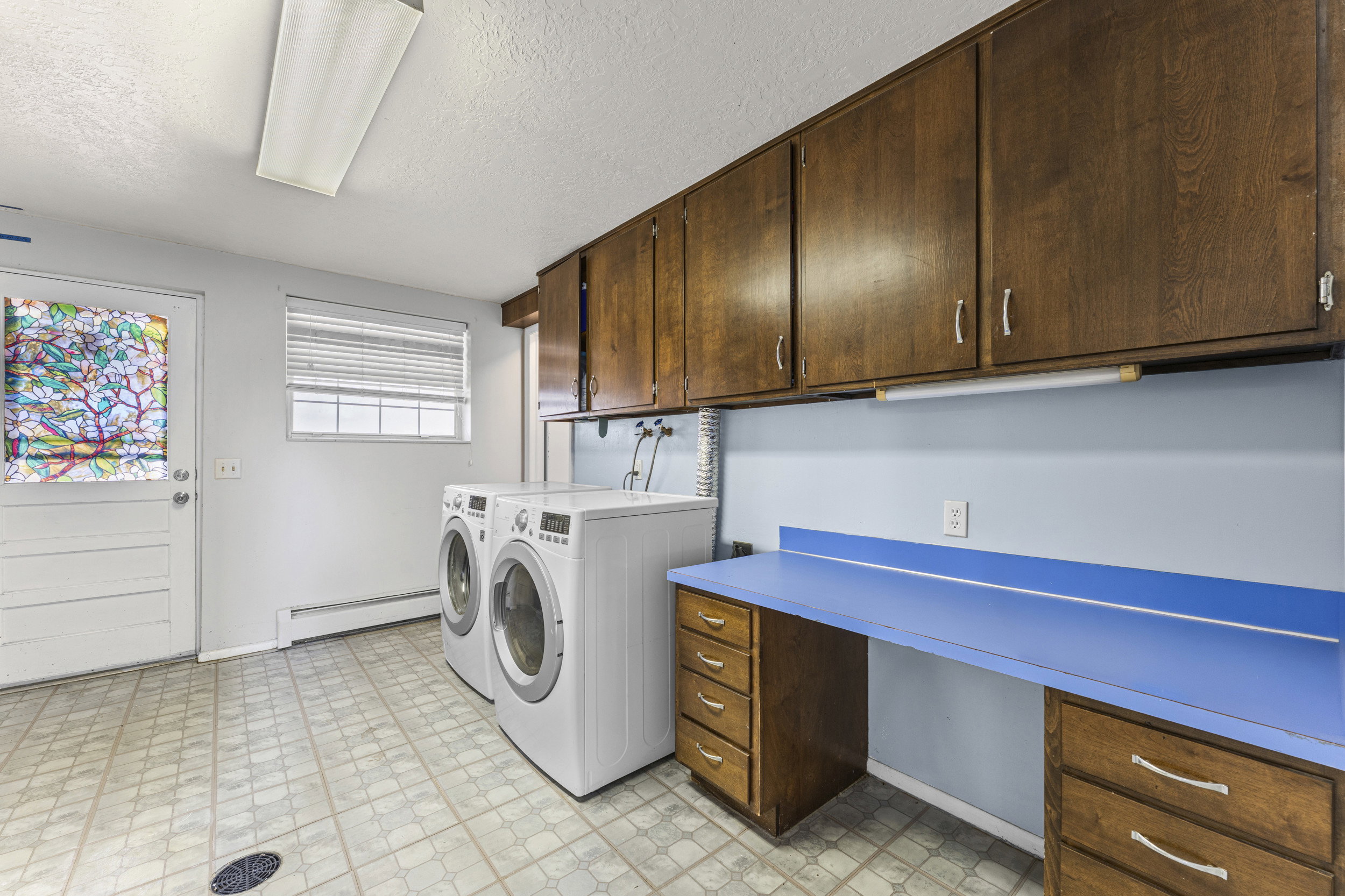 Dedicated laundry area featuring a front-load washer and dryer, ample upper cabinetry, a built-in countertop with integrated drawers, and patterned floor tiling