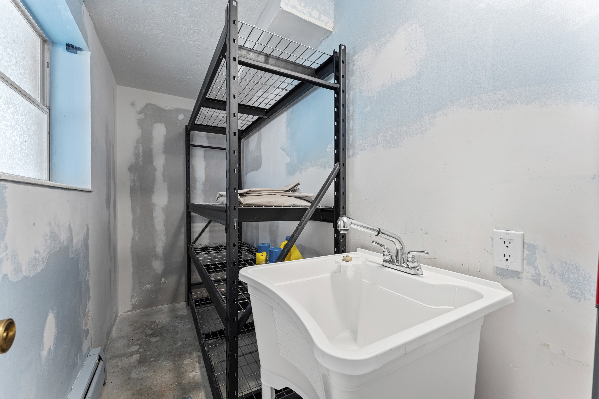 Utility room featuring a laundry sink with chrome faucet, metal shelving, and a single window