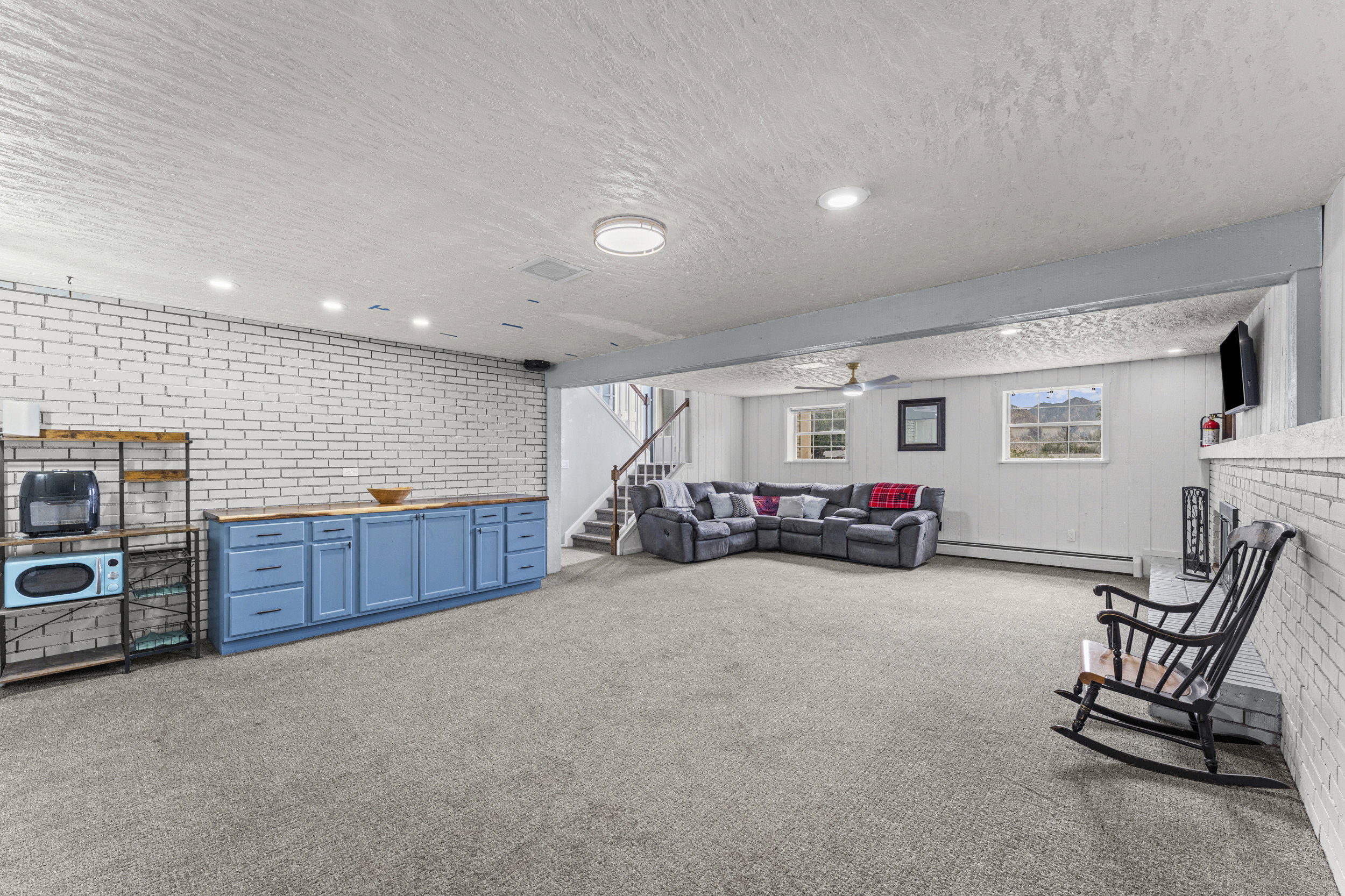 Spacious lower-level living area featuring neutral carpeting, recessed lighting, and a white painted brick accent wall