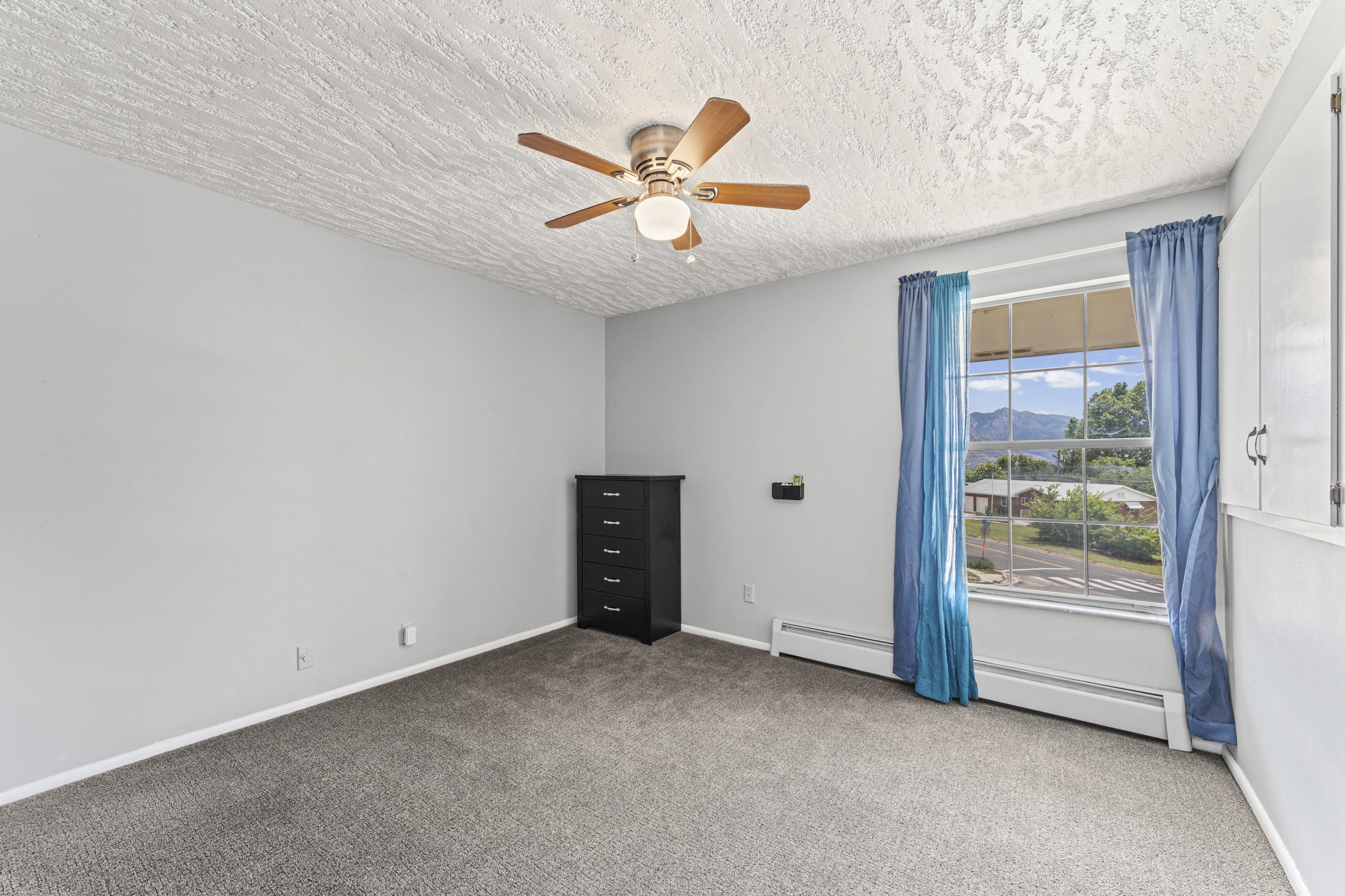 Carpeted room featuring a ceiling fan with light fixture, a large window, and built-in white cabinetry