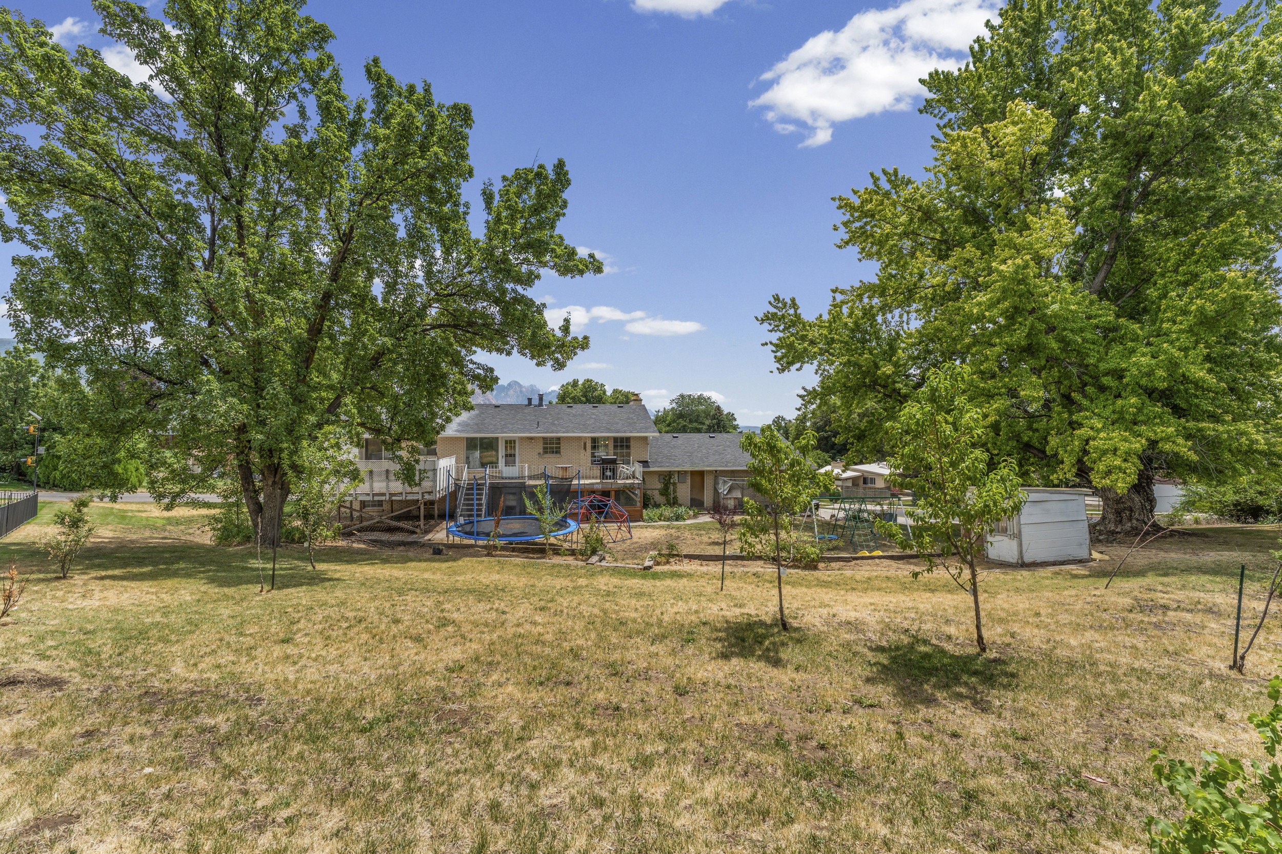 Expansive backyard featuring mature trees, a multi-level deck, and a white storage shed