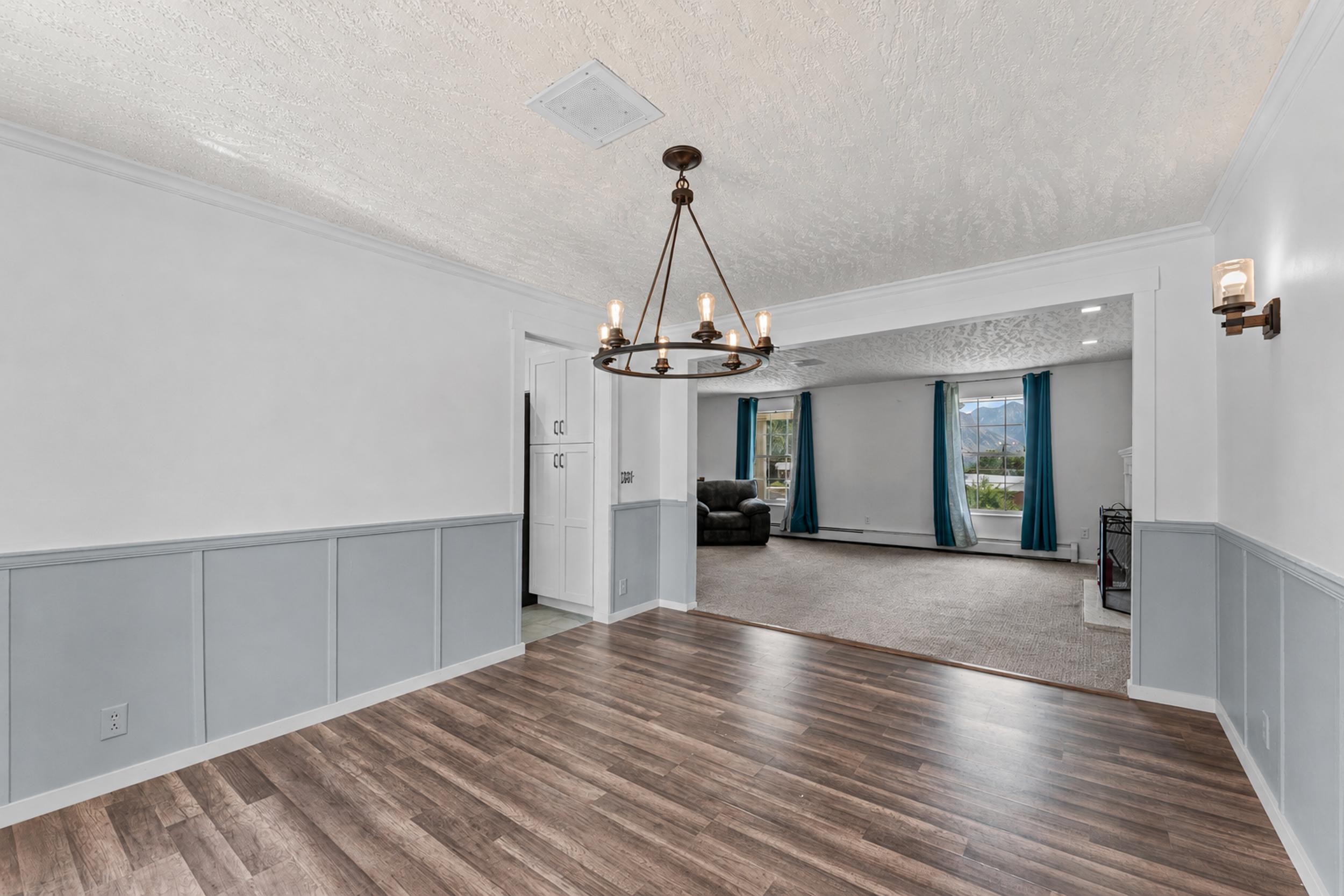 Spacious interior featuring wood-finish flooring, wainscoting with crown molding, a multi-light chandelier, and an archway opening to an additional carpeted room