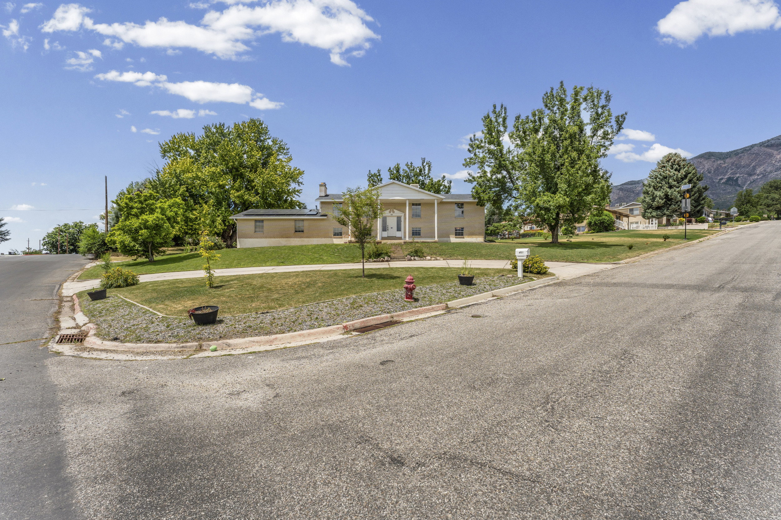 Expansive corner lot featuring a stucco exterior, mature trees, a manicured lawn, and mountain scenery