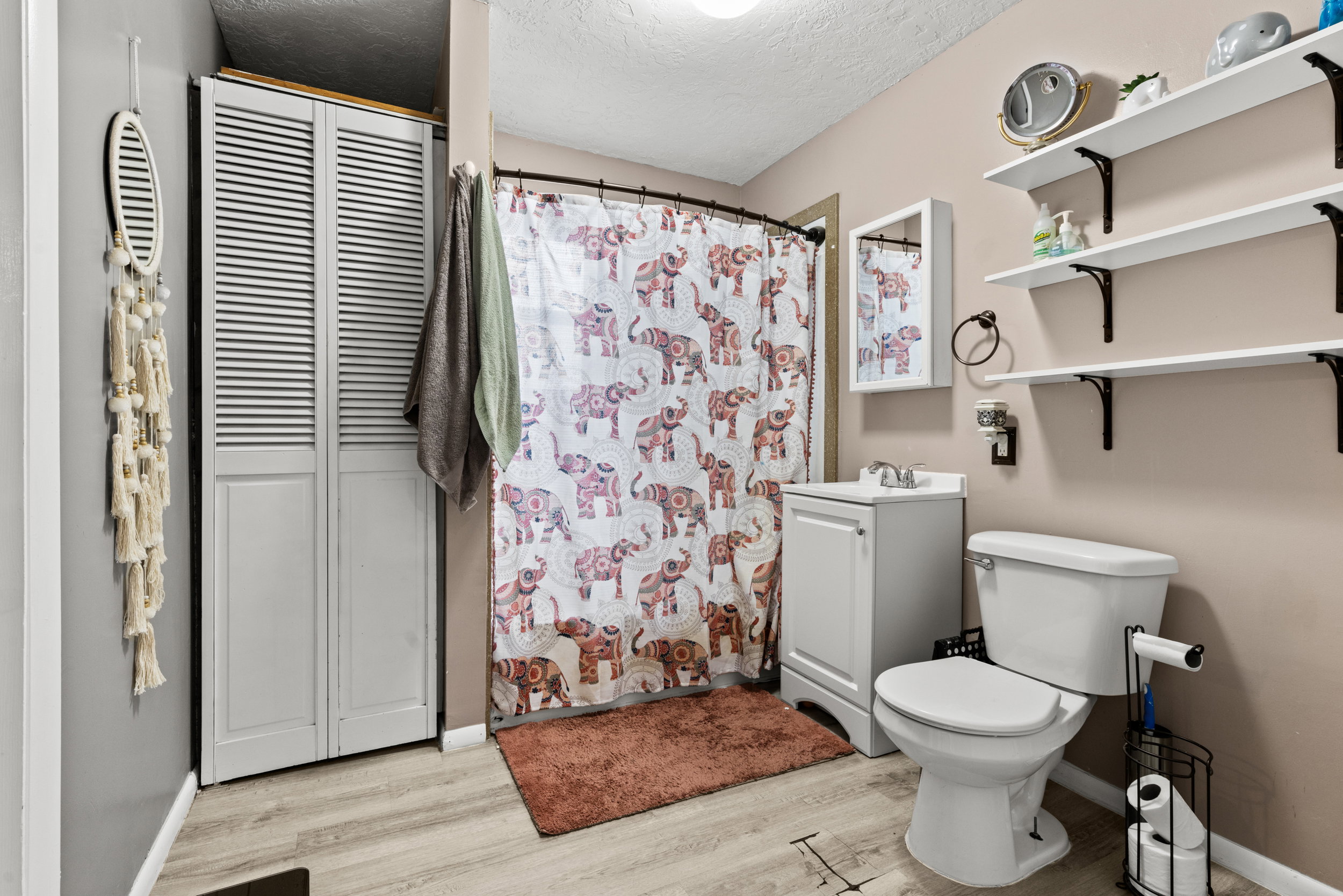 Bathroom with wood-finish flooring, a white vanity with integrated sink, and white shelving with dark brackets