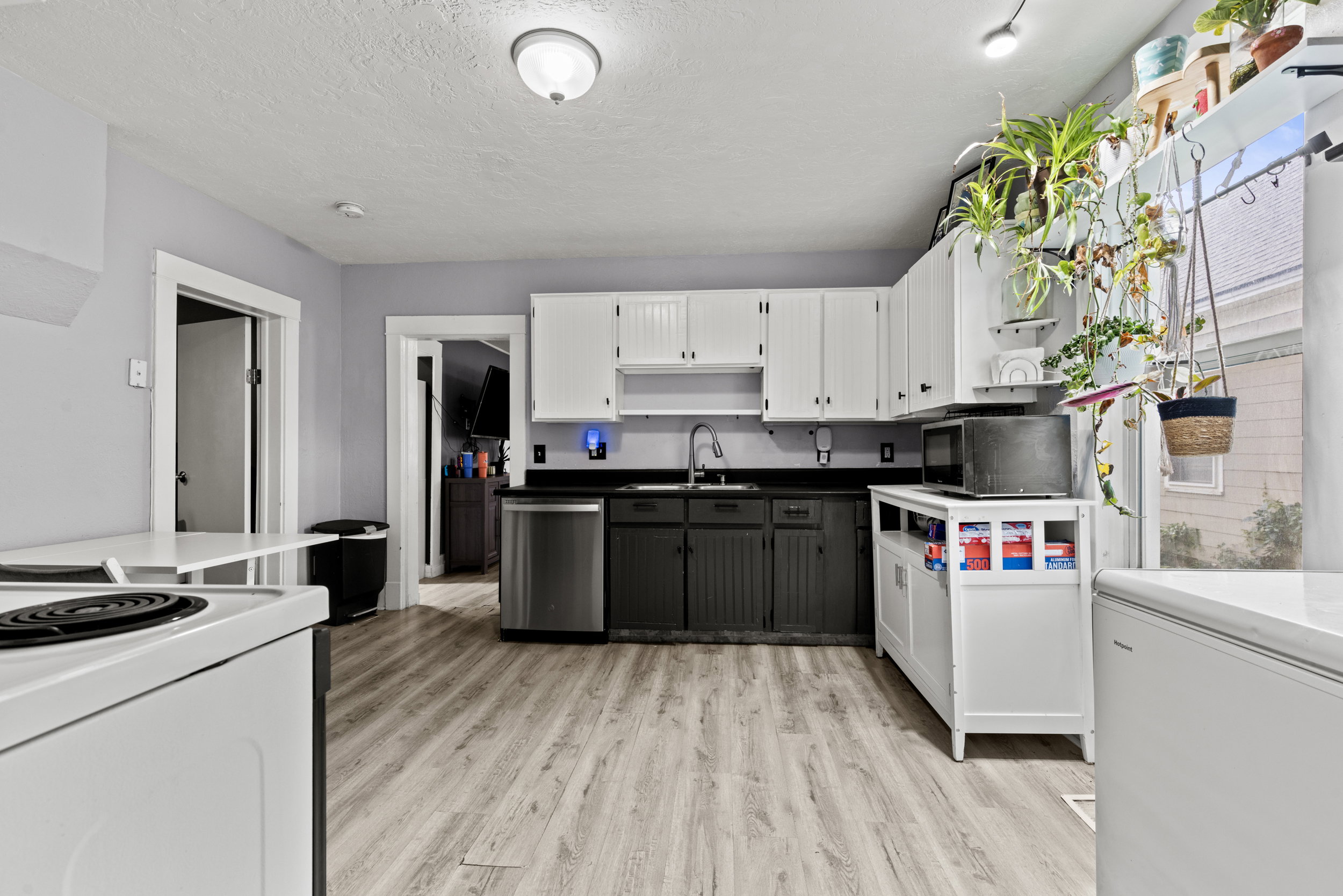 Kitchen featuring wood-finish flooring, two-tone cabinetry with white upper and dark lower units, a stainless steel dishwasher, and a window providing natural light