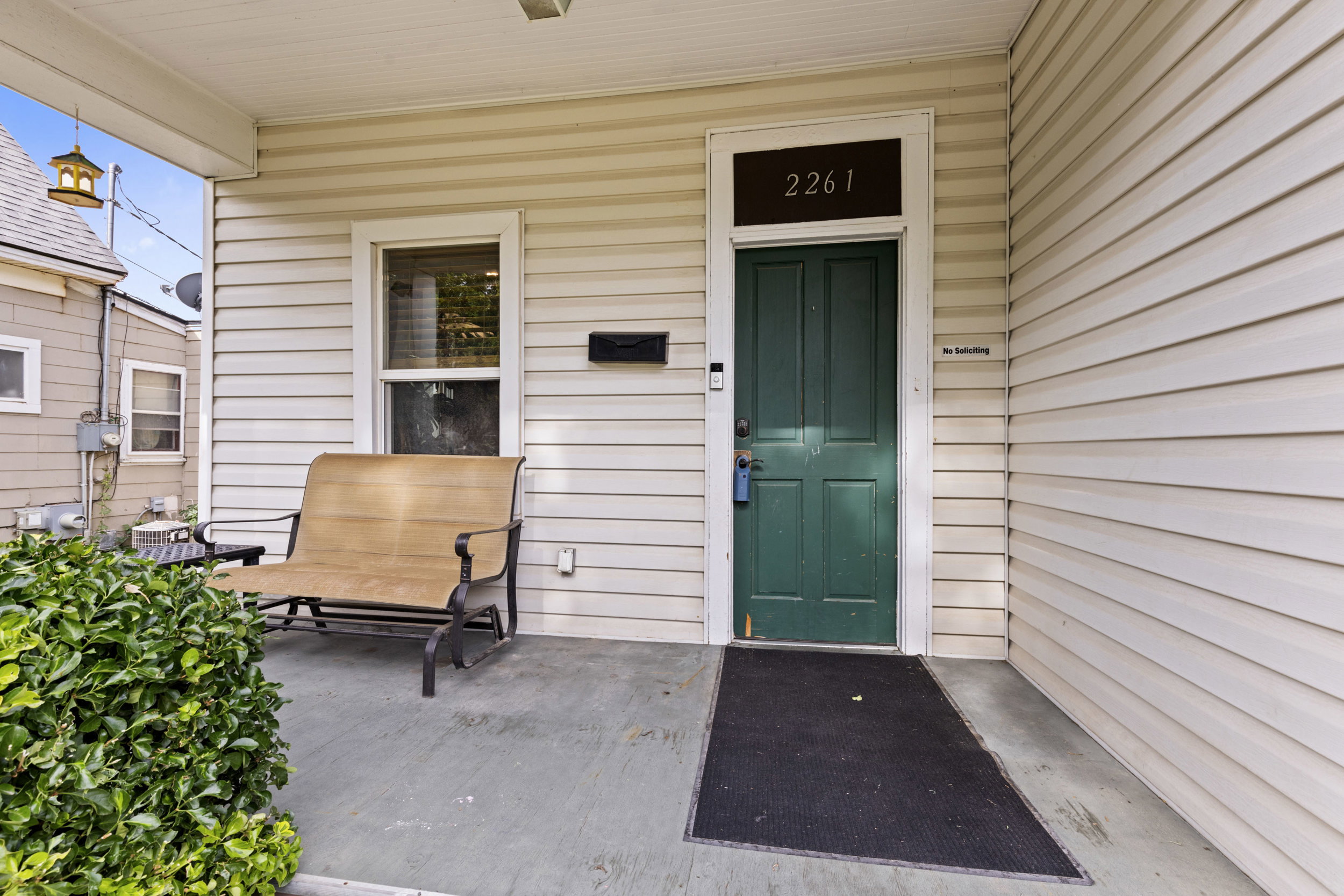 Covered front porch featuring cream-colored siding and a dark green entry door with transom window