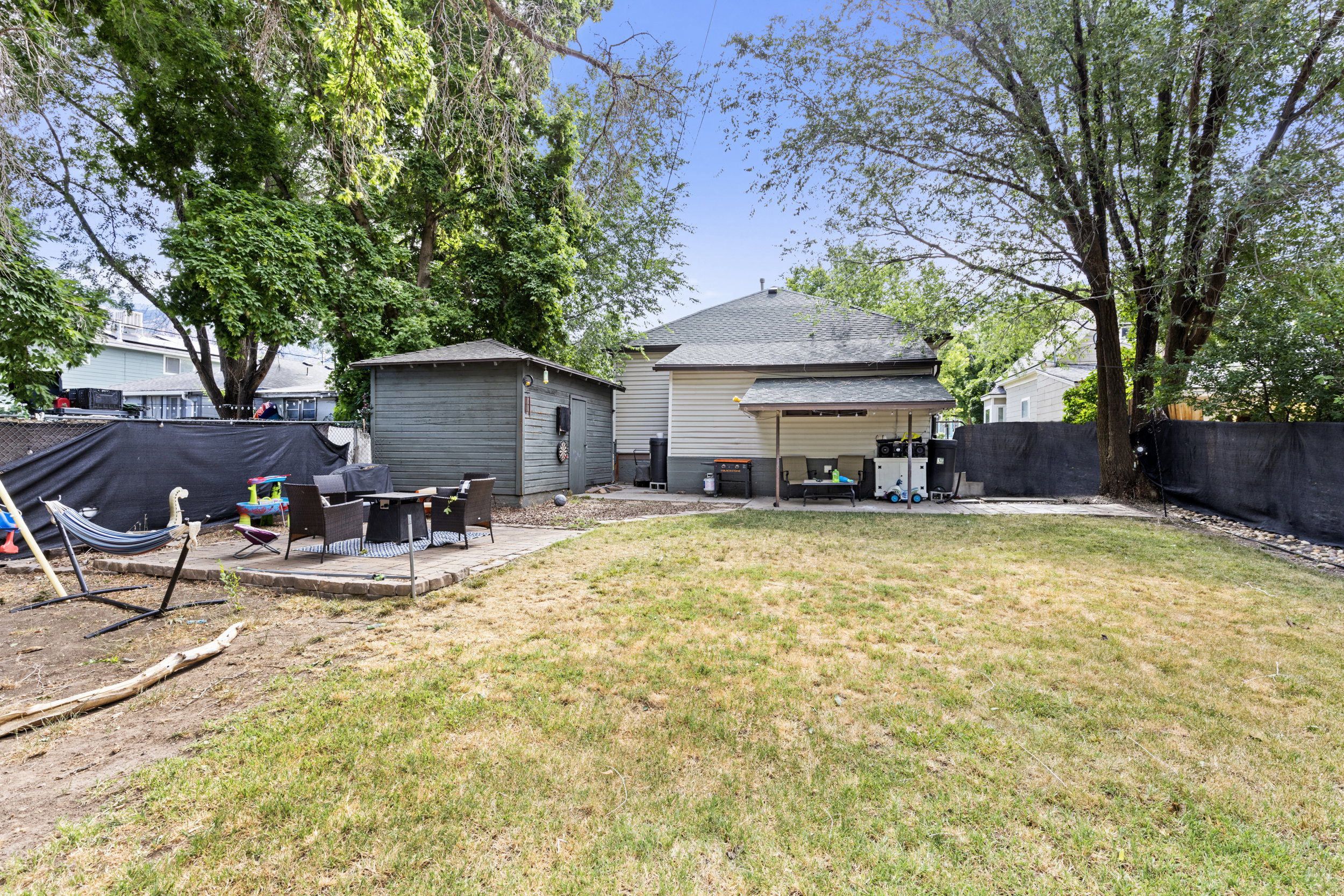 Expansive backyard featuring a large grass area, a dedicated patio space, a covered back porch, a storage shed, and mature trees