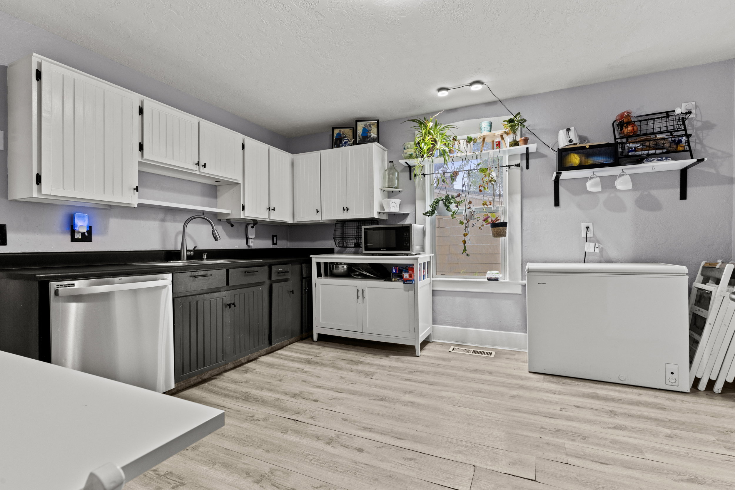 Kitchen featuring wood-finish flooring, two-tone cabinetry with black countertops, and a stainless steel dishwasher