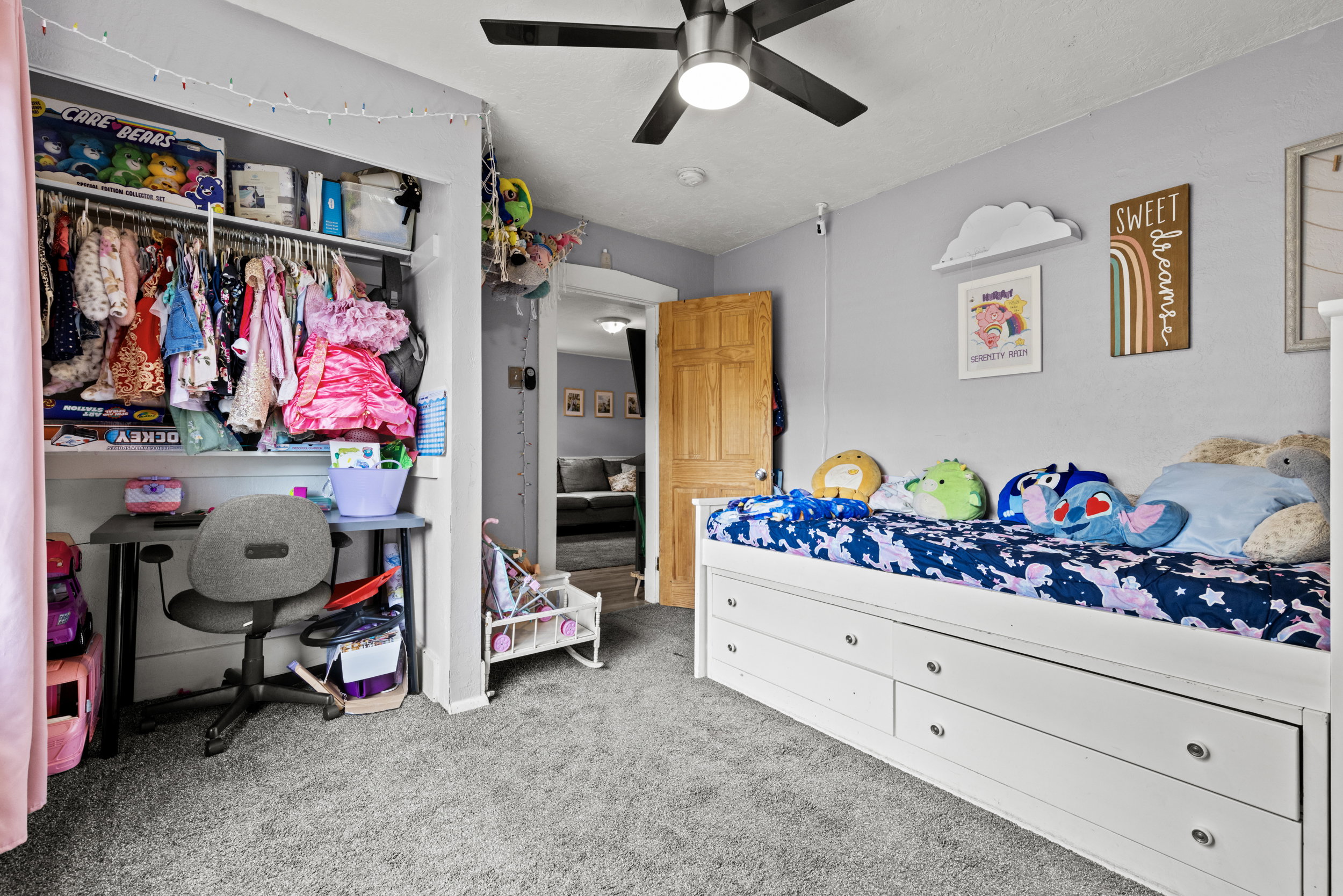 Carpeted room featuring a ceiling fan with integrated lighting, a built-in closet with shelving and hanging rods, a light wood-finish door, and pale gray wall finishes
