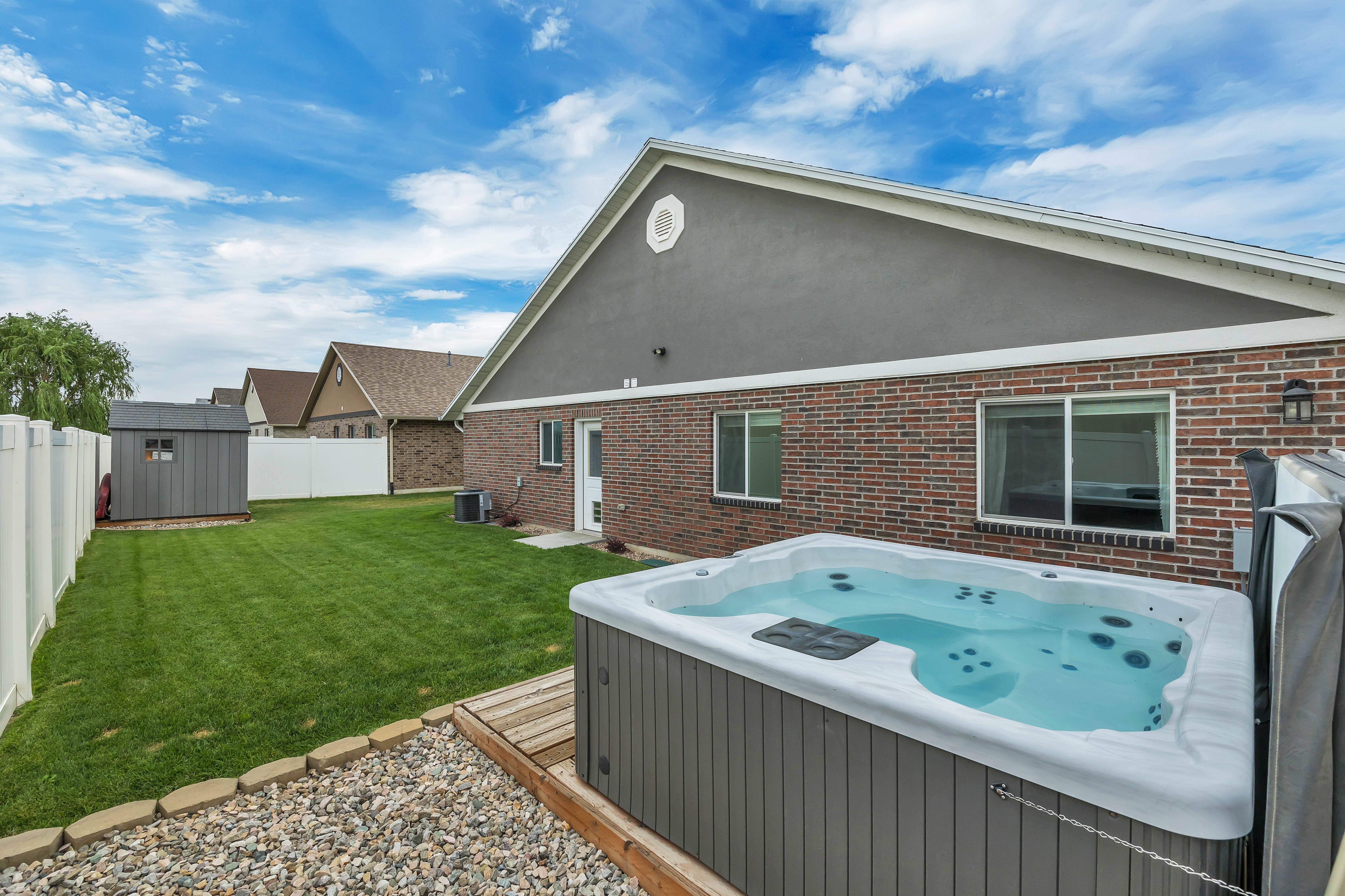 Expansive backyard featuring a built-in spa, manicured lawn, and white vinyl privacy fencing