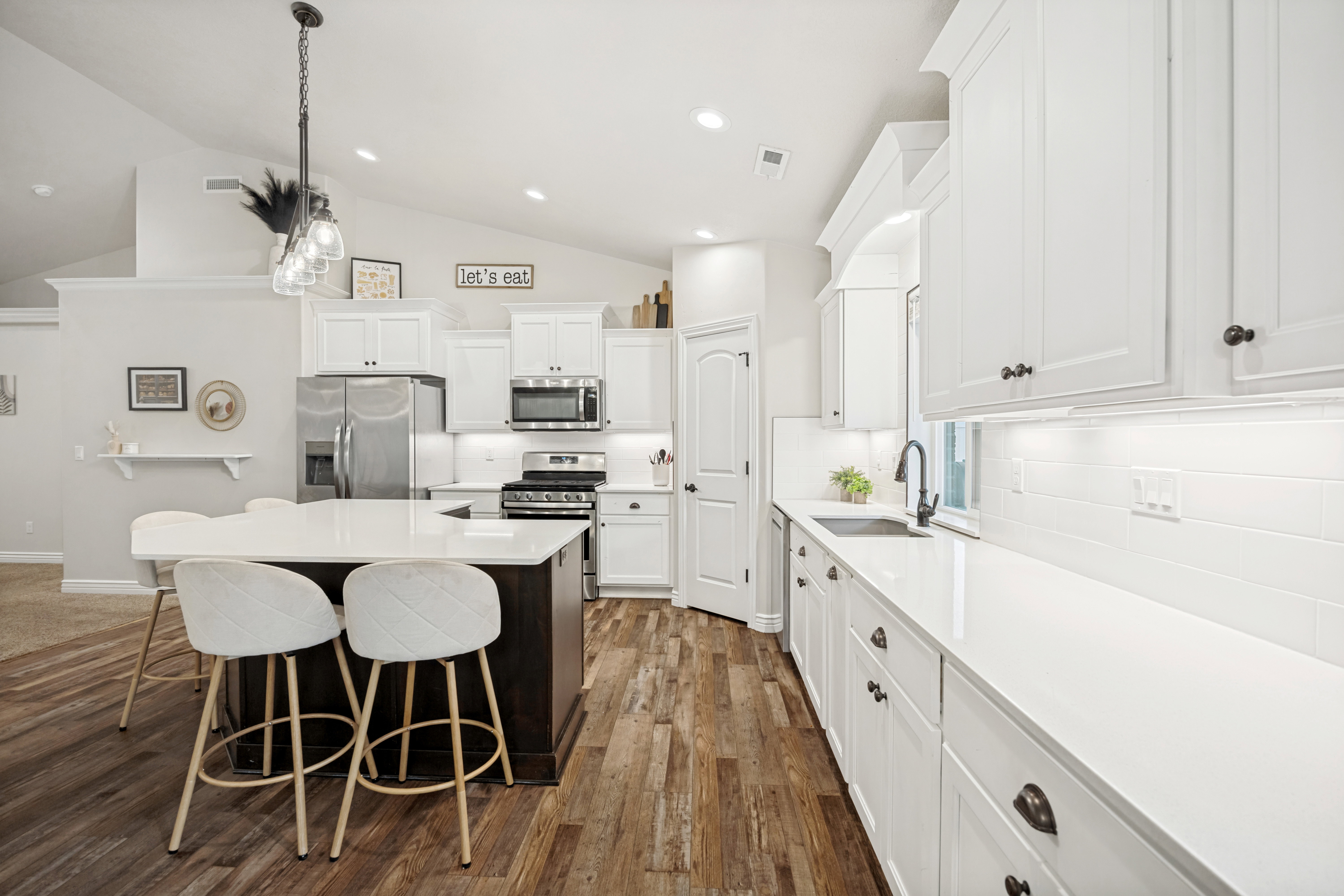 Kitchen featuring a dark wood-finish island with a light-toned countertop, white cabinetry with dark hardware, stainless steel appliances, and wood-finish flooring