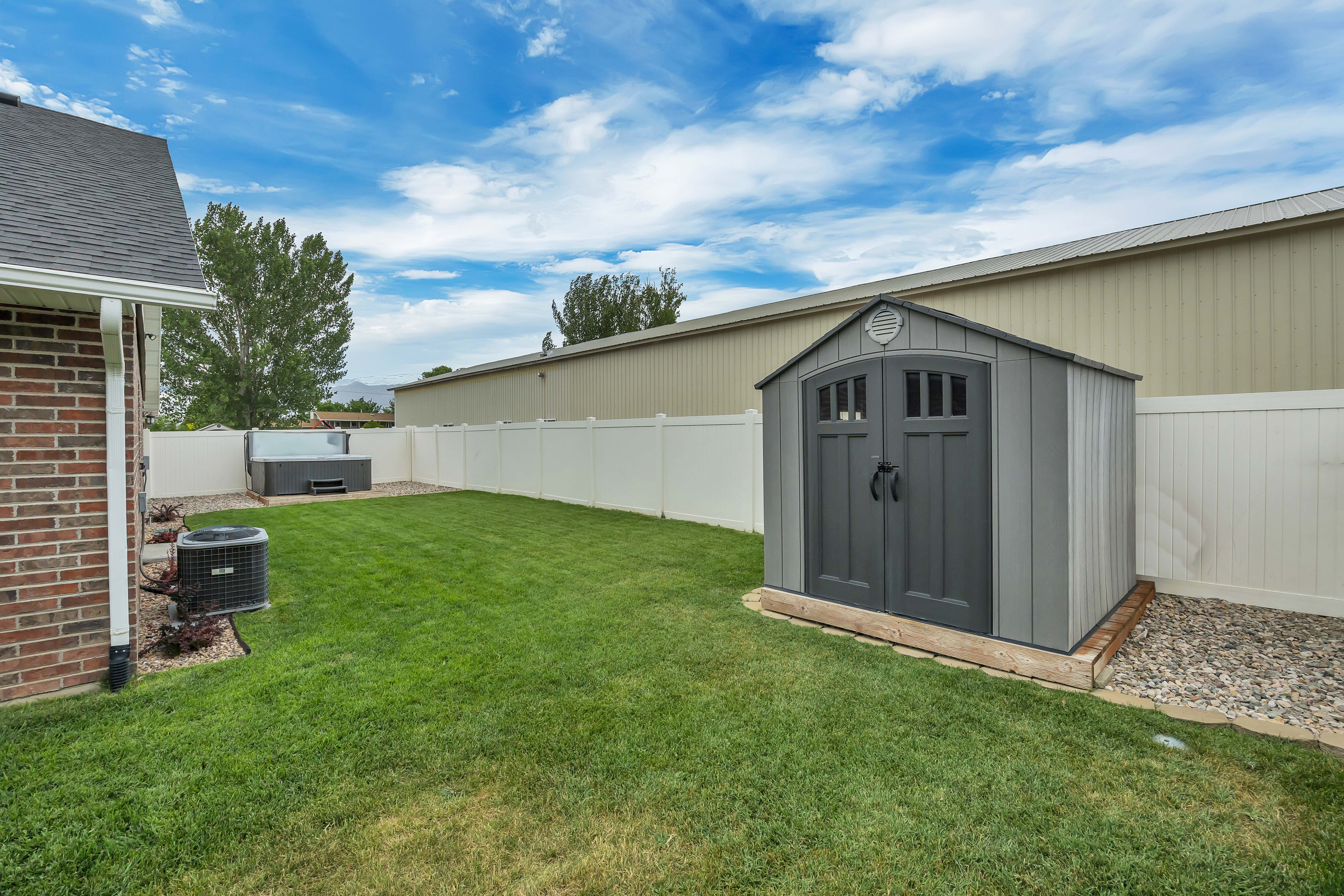 Expansive backyard featuring a manicured lawn, white vinyl fencing, and a built-in storage shed with double doors