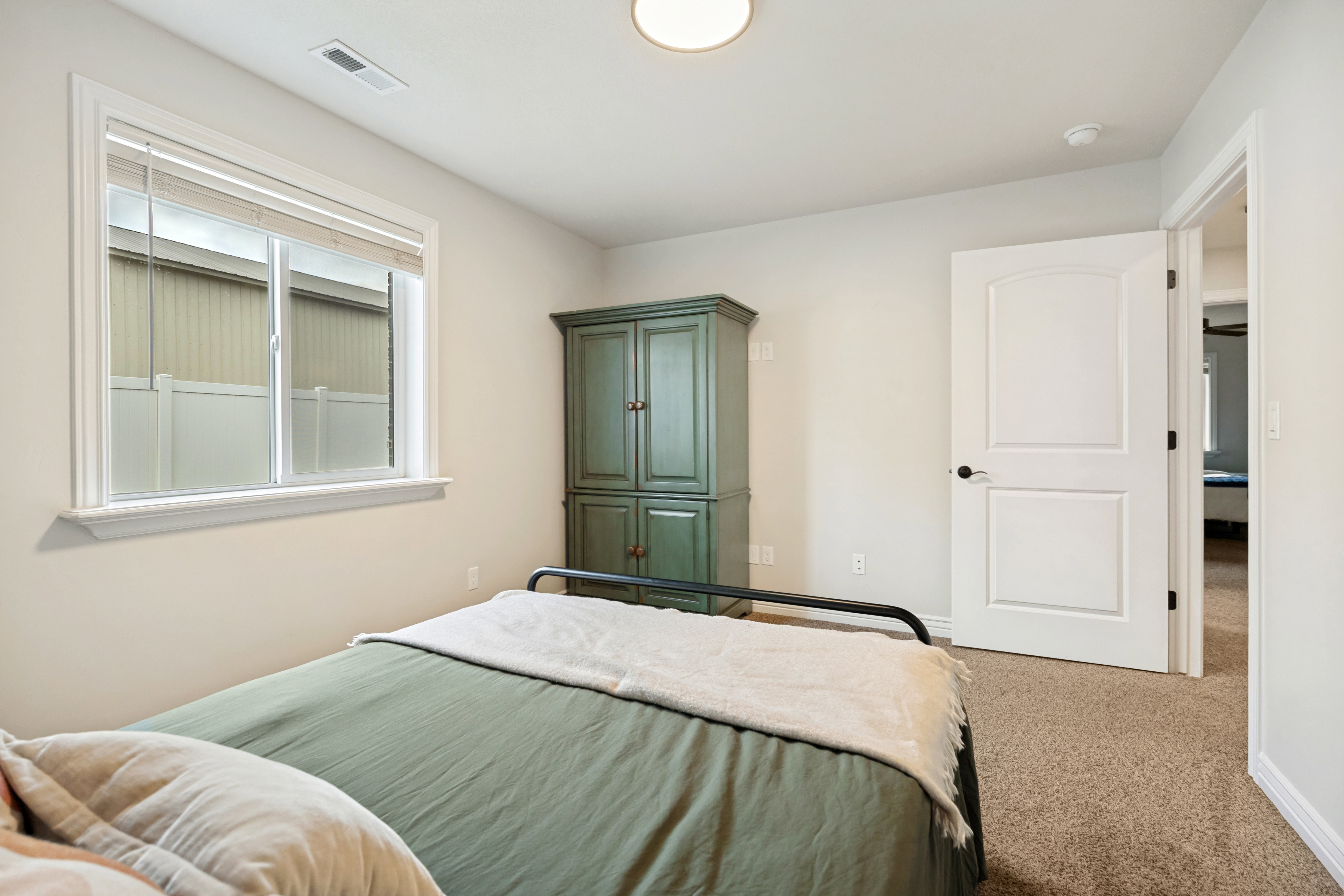 Bedroom featuring light neutral wall paint, a window with blinds, carpet flooring, a flush-mount ceiling light, and a two-panel interior door with black hardware