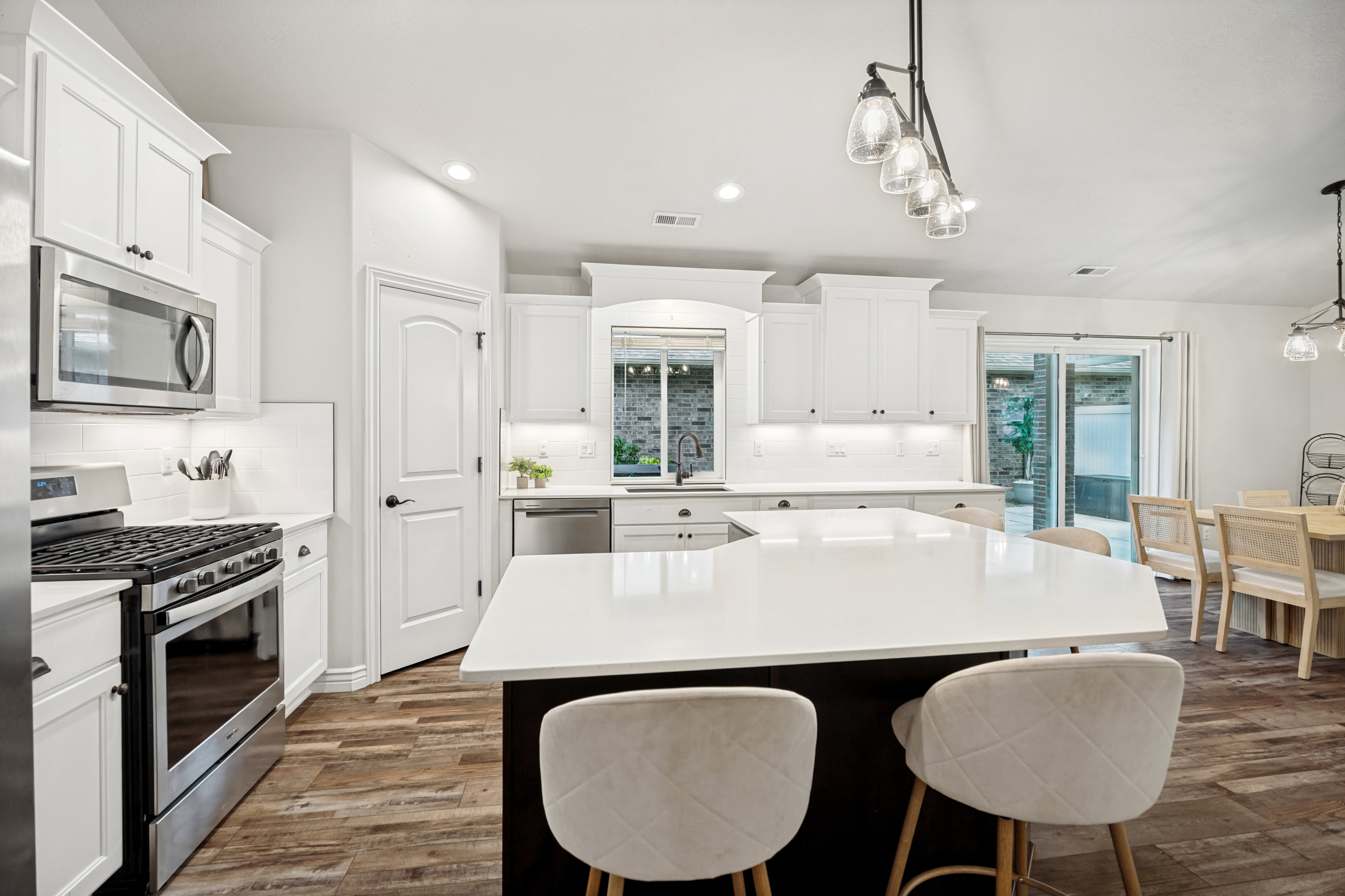 Modern kitchen featuring white cabinetry, stainless steel appliances, a white quartz island, wood-finish flooring, and recessed lighting