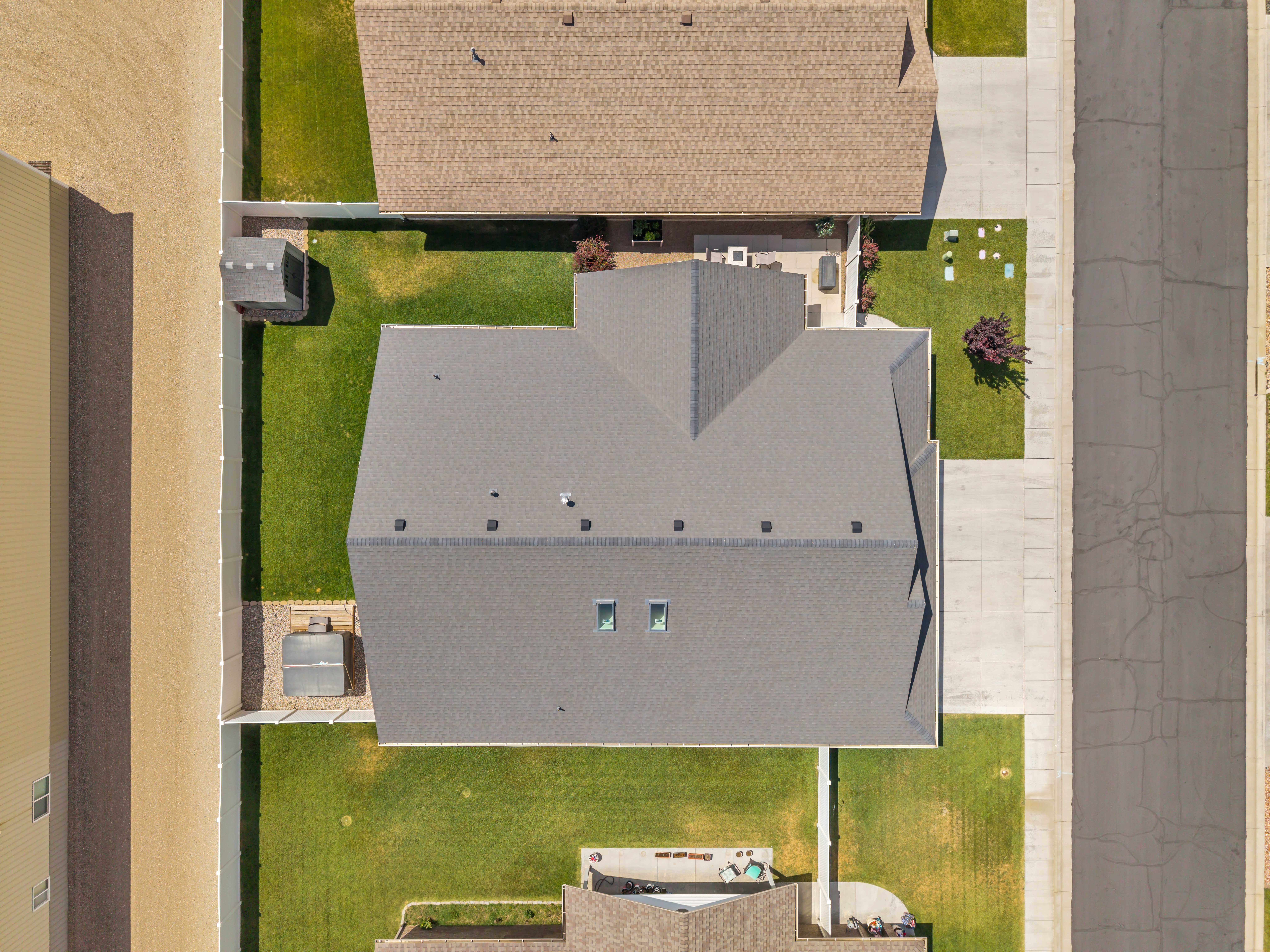 Aerial view showcasing a gray shingle roof, green lawn, concrete driveway, and a fenced perimeter