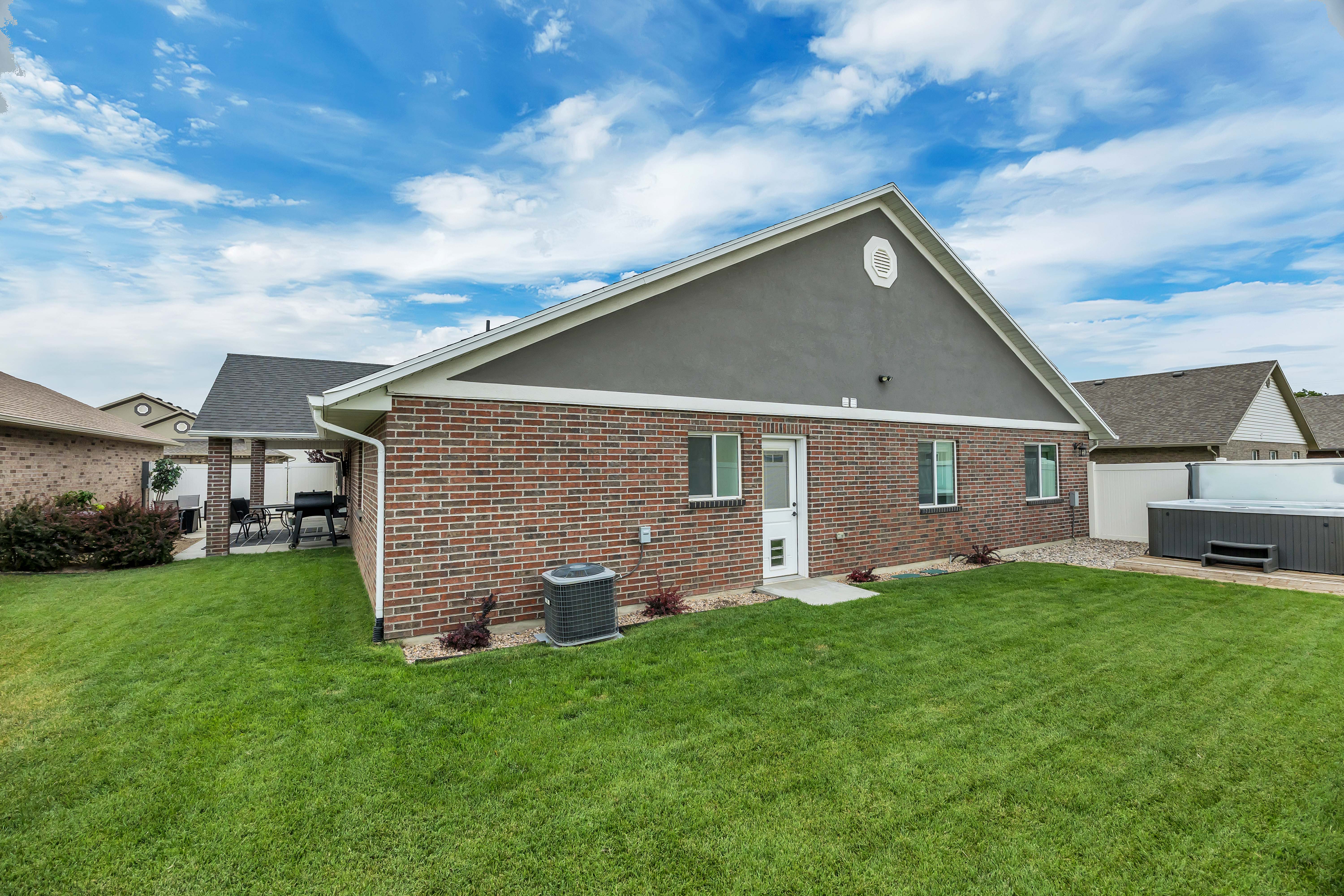 Expansive rear yard featuring a manicured lawn, brick and stucco exterior, covered patio, and privacy fencing
