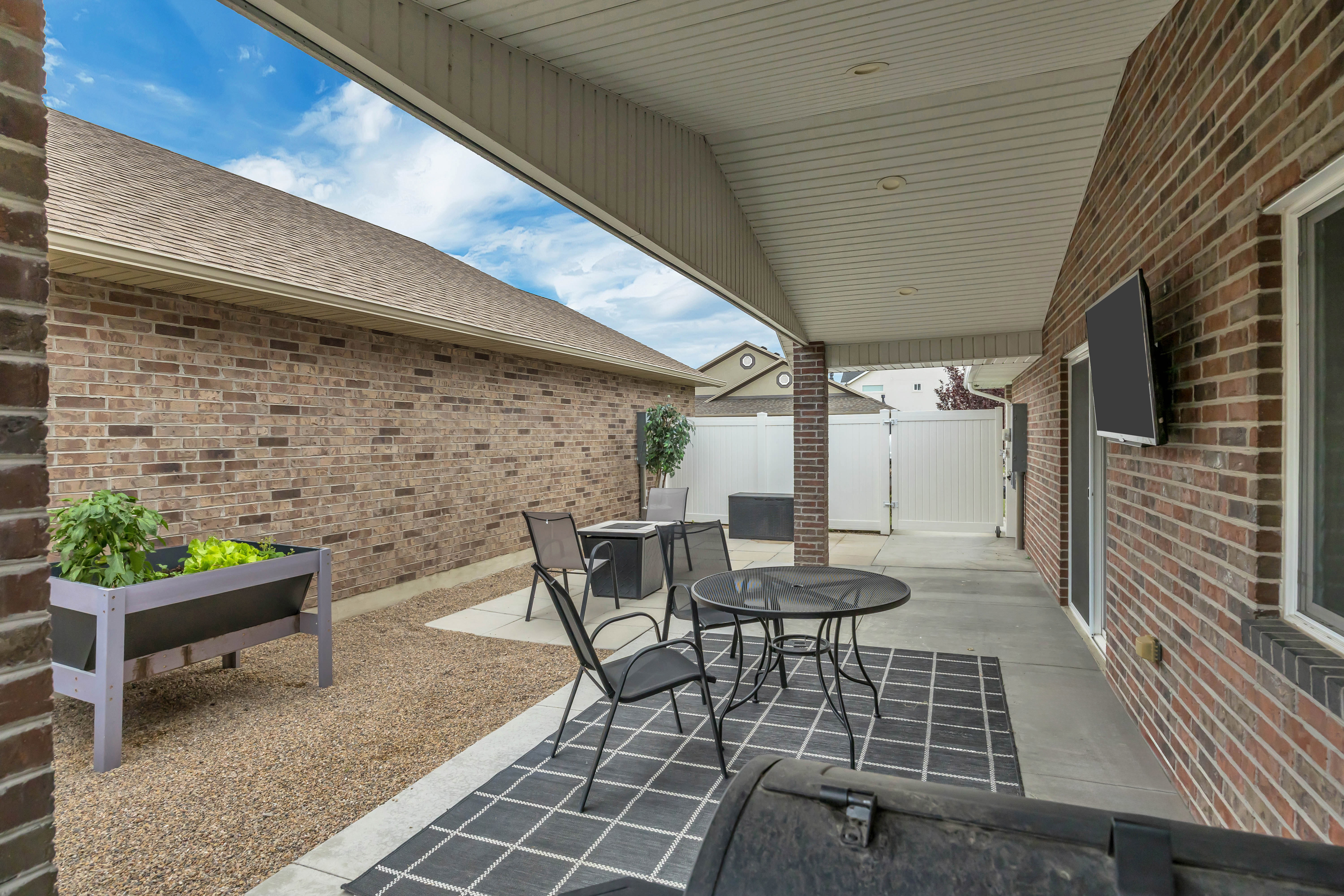 Covered concrete patio featuring brick pillars, recessed lighting, and a mounted outdoor television