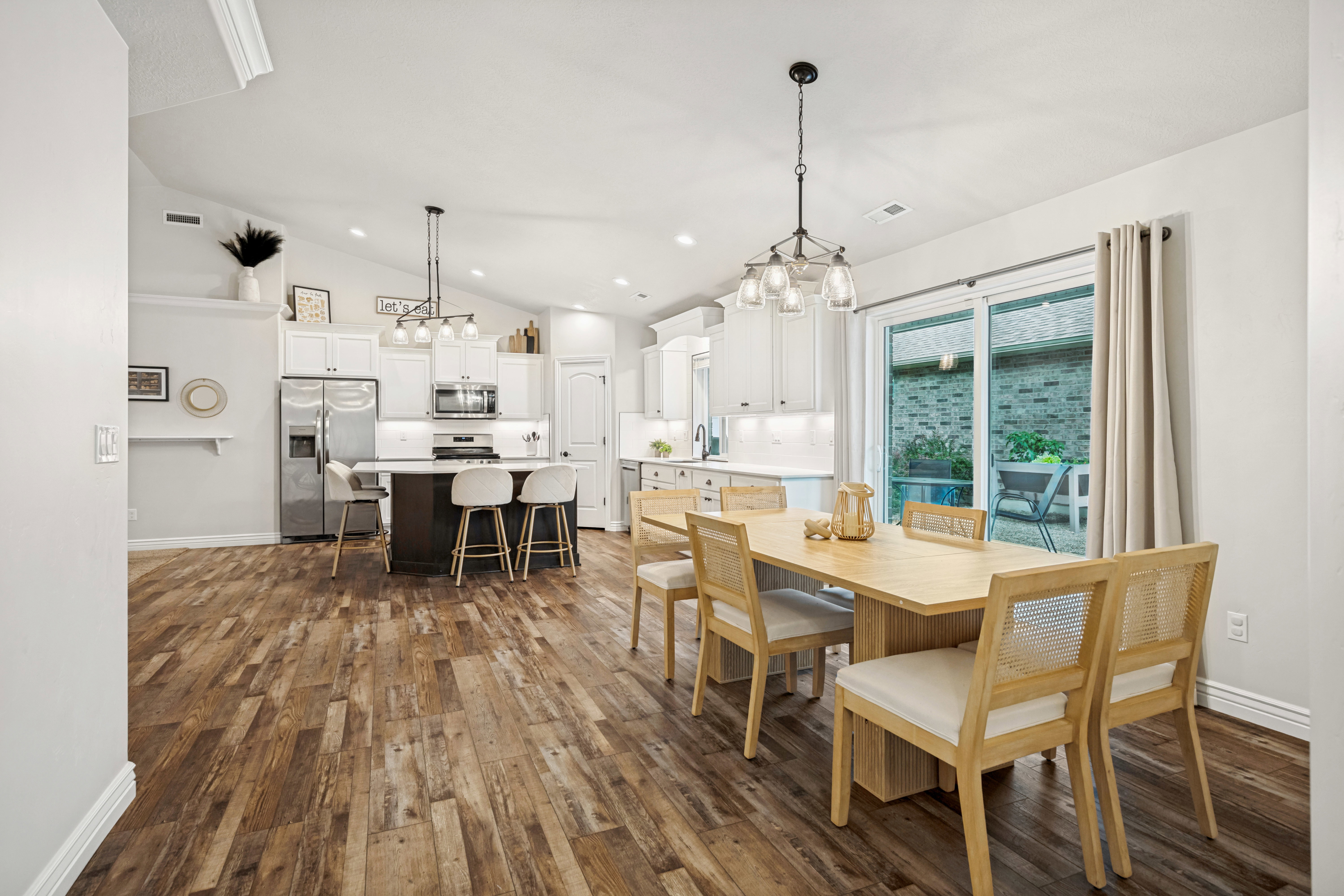 Open-concept dining area featuring wood-finish flooring, a contemporary chandelier, and direct access to the outdoor patio via sliding glass doors