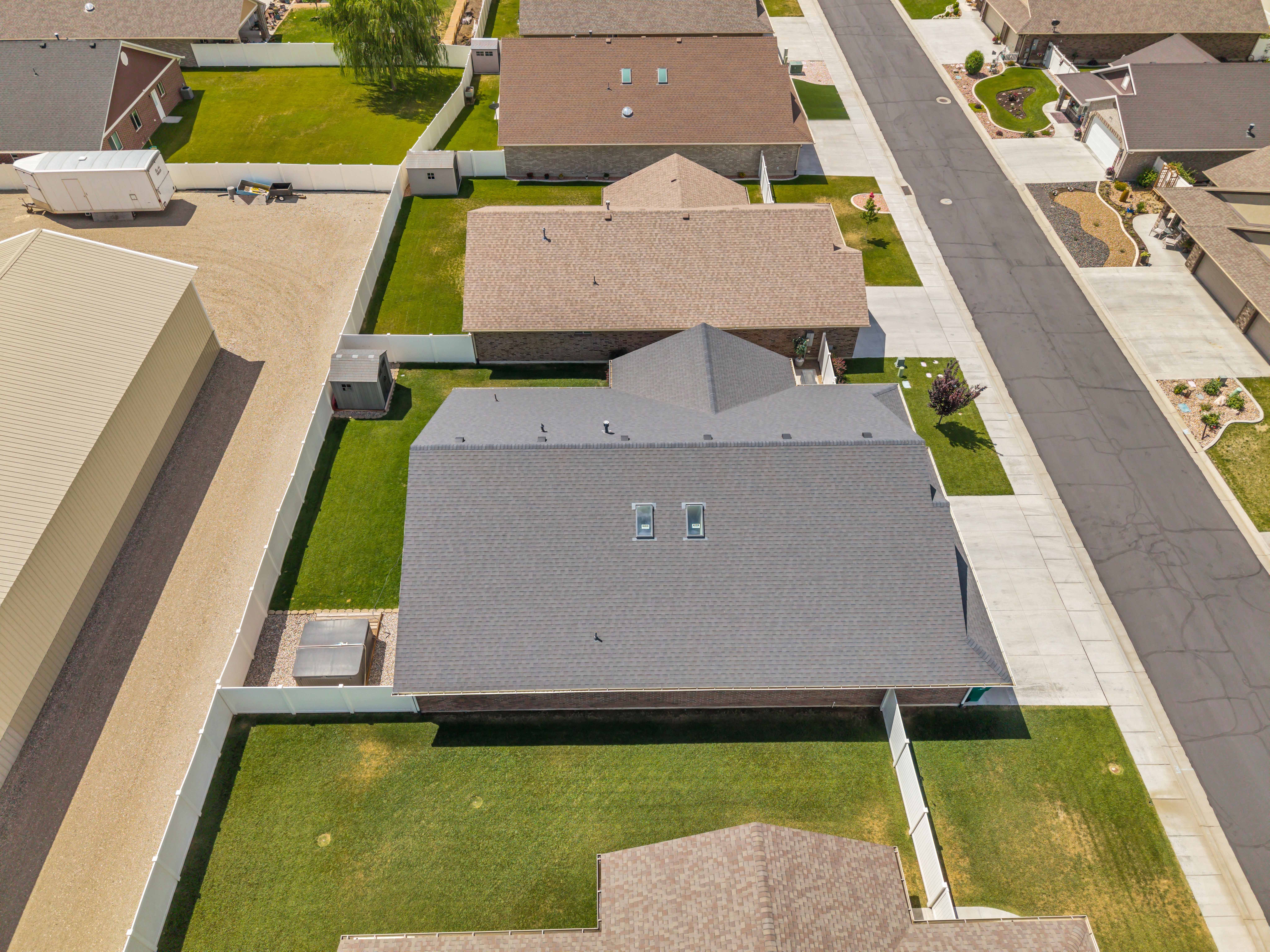 Property featuring a dark gray shingle roof, a white perimeter fence, and a green lawn