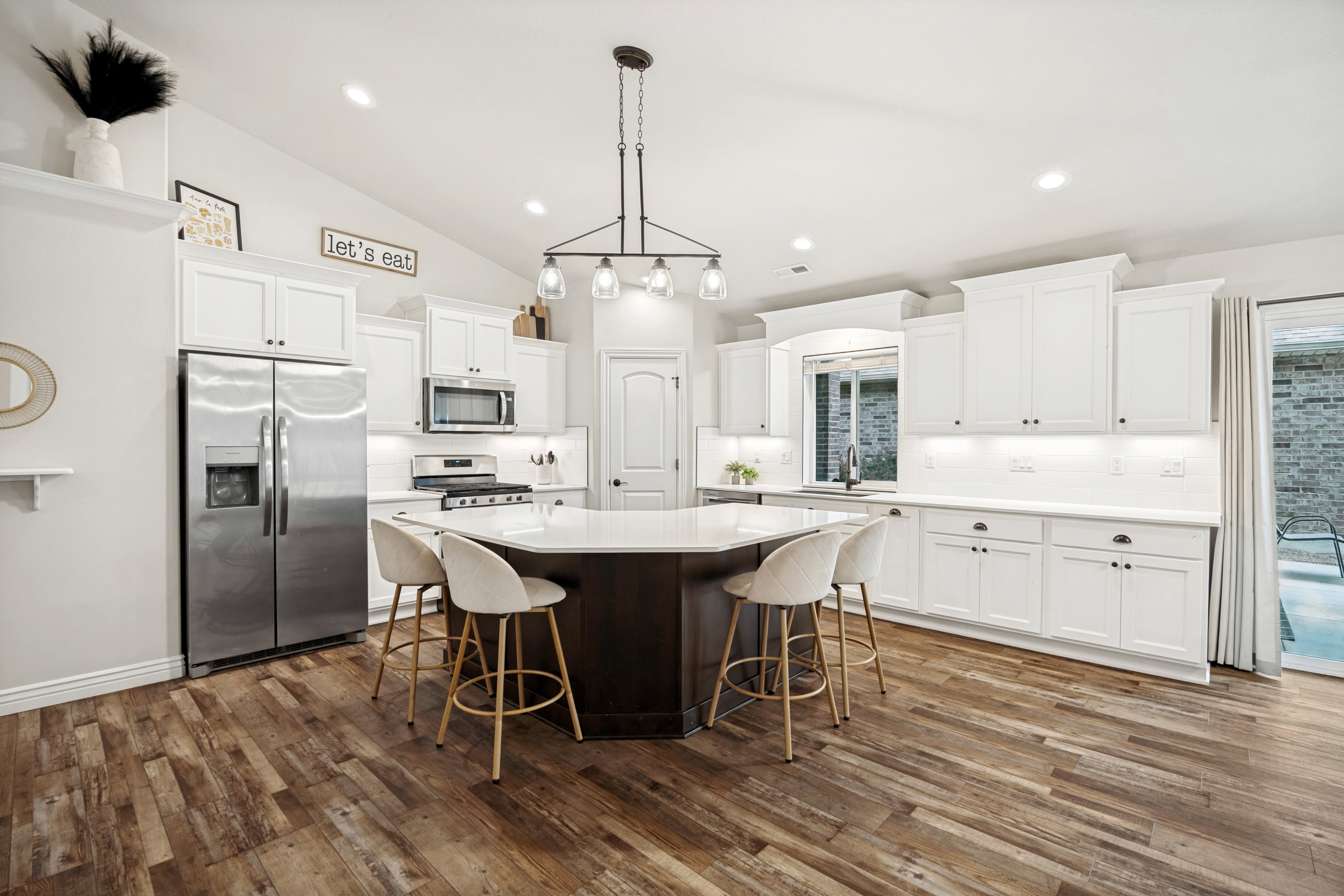 Spacious kitchen featuring white shaker cabinetry, stainless steel appliances, a multi-sided island with seating, recessed lighting, and wood-finish flooring