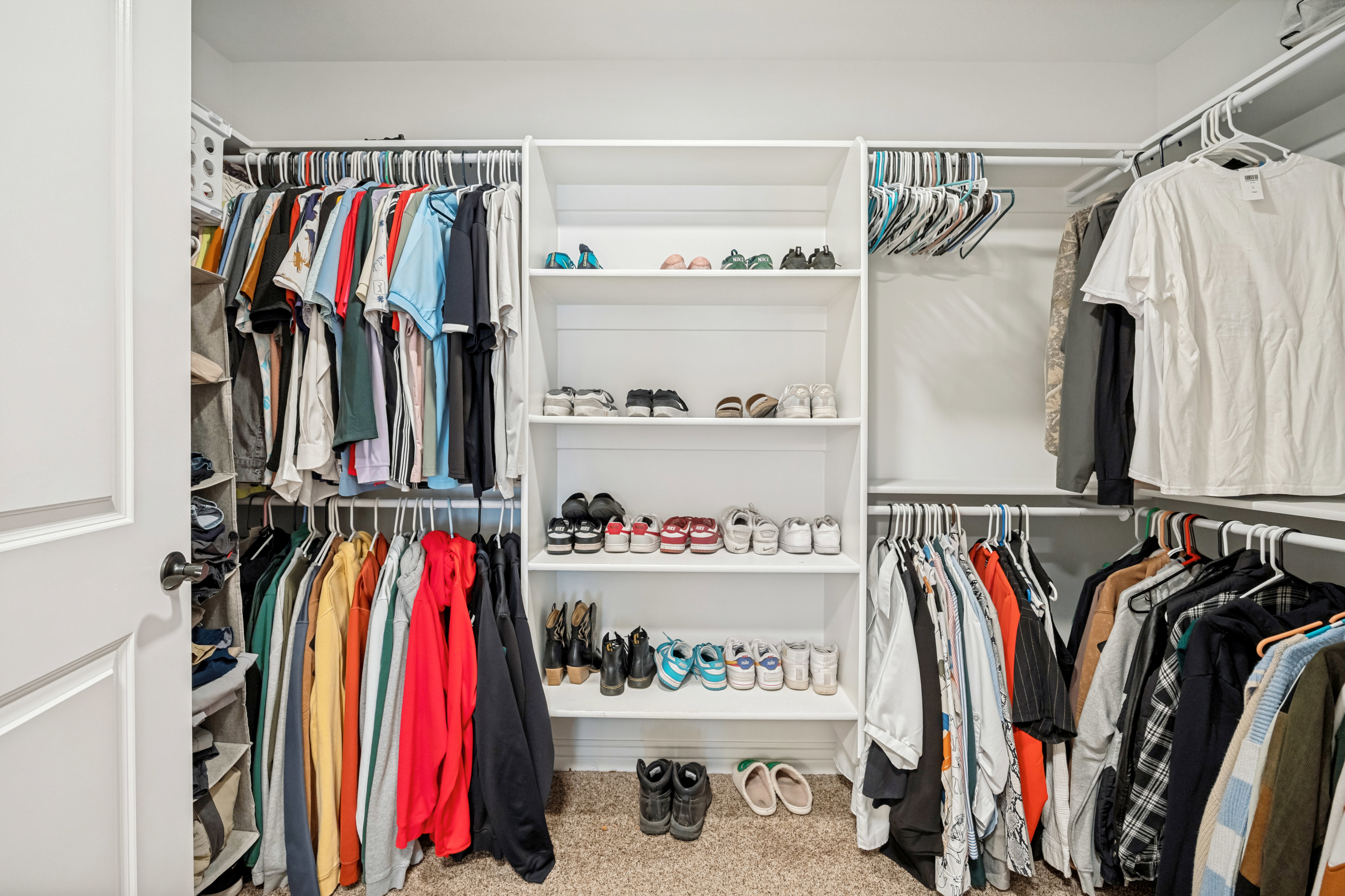 Walk-in closet featuring built-in white shelving, multiple hanging rods, and carpet flooring