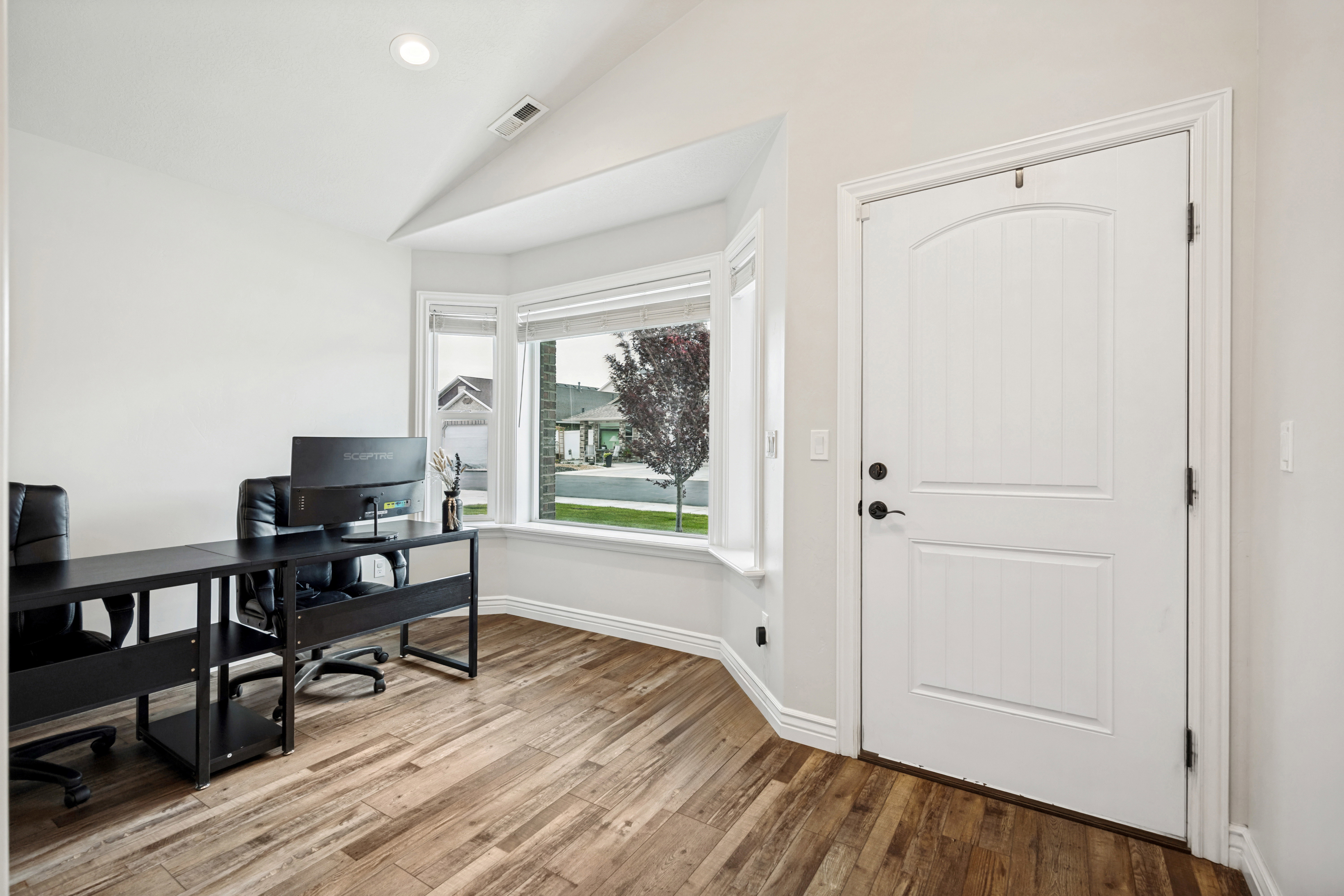 Spacious room featuring wood-finish flooring, a bright bay window, recessed lighting, and a vaulted ceiling
