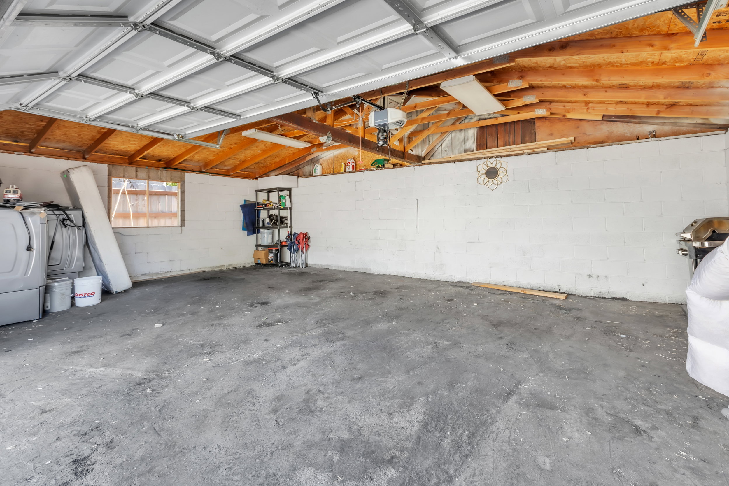 Spacious garage with exposed wood beam ceiling, concrete flooring, and a single pane window