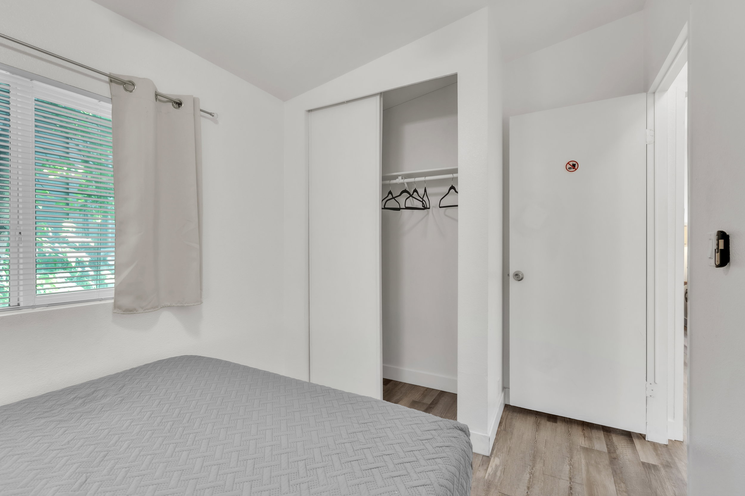 Bedroom featuring a window with blinds, light-toned walls, and wood-finish flooring