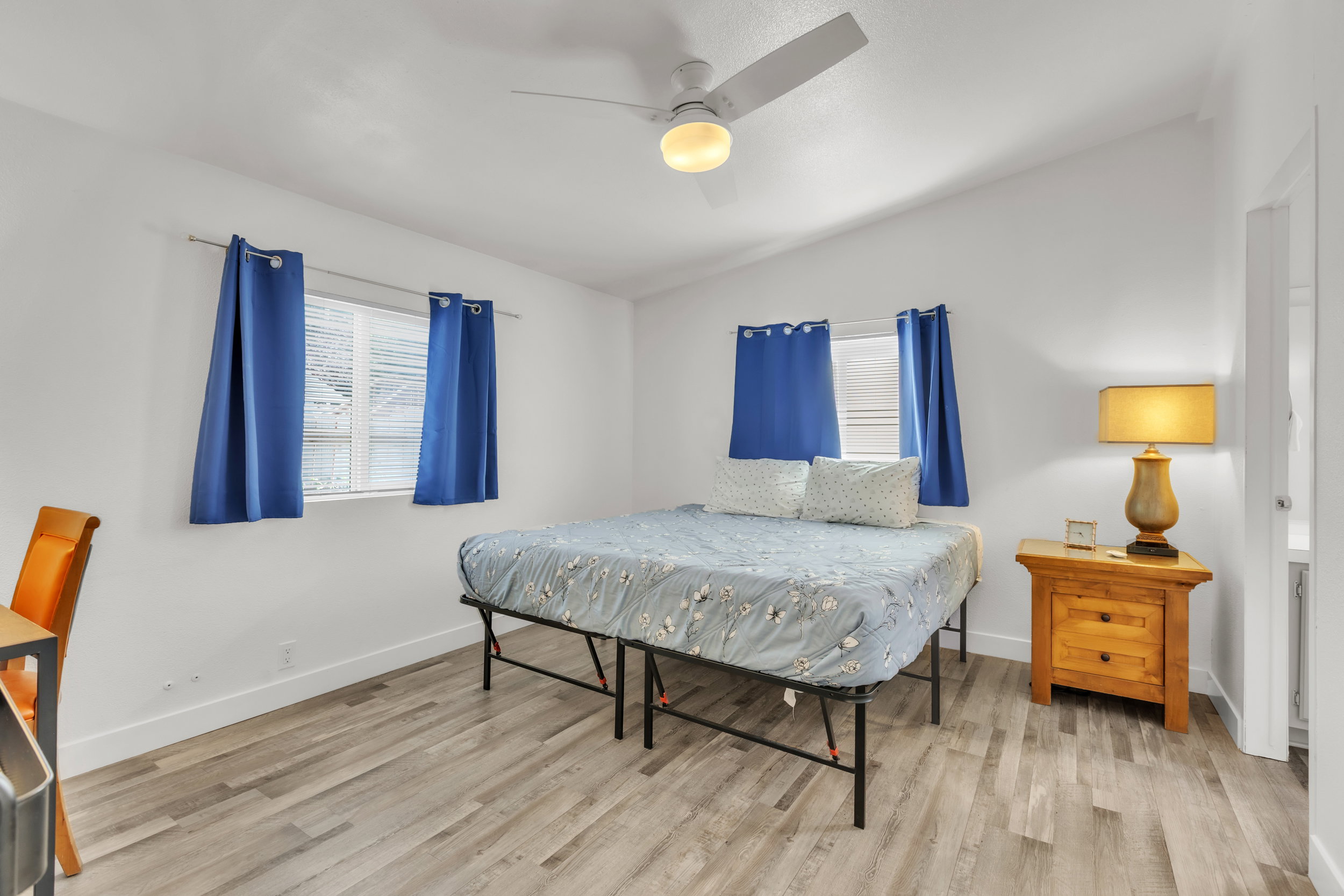 Room featuring vaulted ceiling, wood-finish flooring, two windows with blinds, a ceiling fan with integrated lighting, and white baseboards