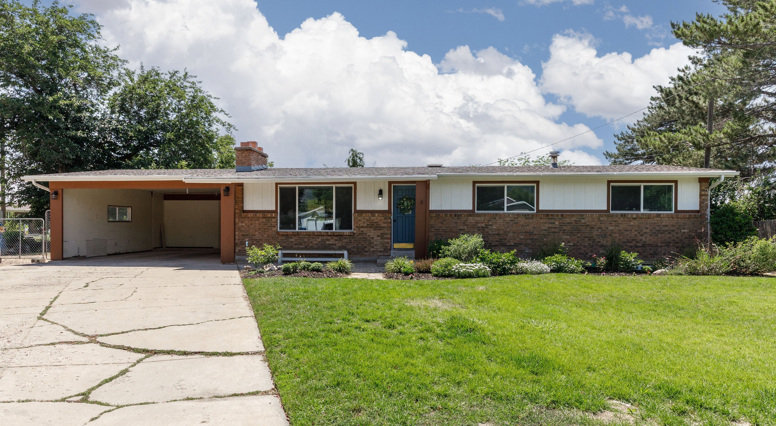 Brick-clad single-story home featuring a carport, a front lawn, and established landscaping