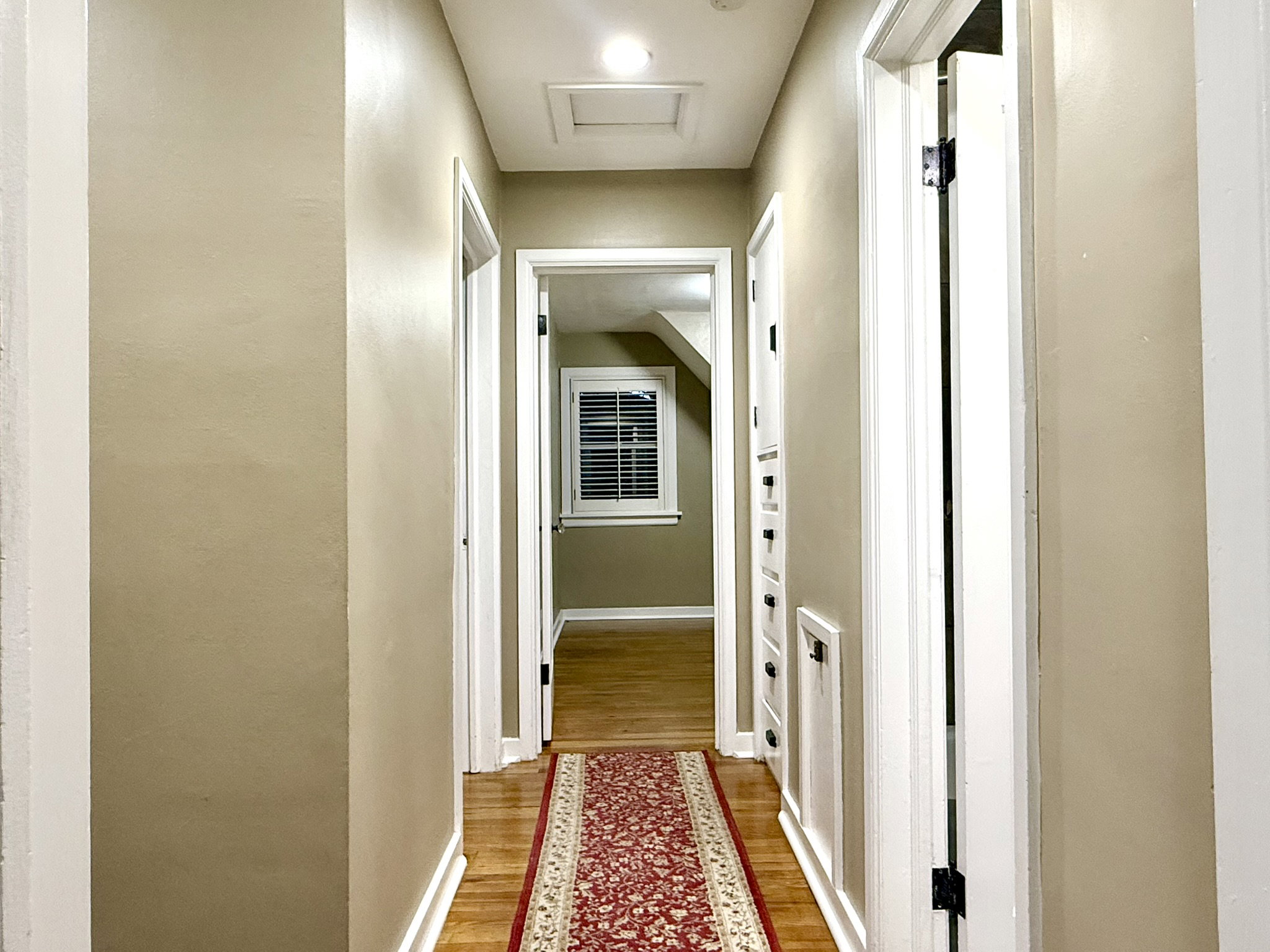 Hallway  between Bedrooms & Bathroom featuring wood-finish flooring, light tan walls, white trim, and a ceiling access panel