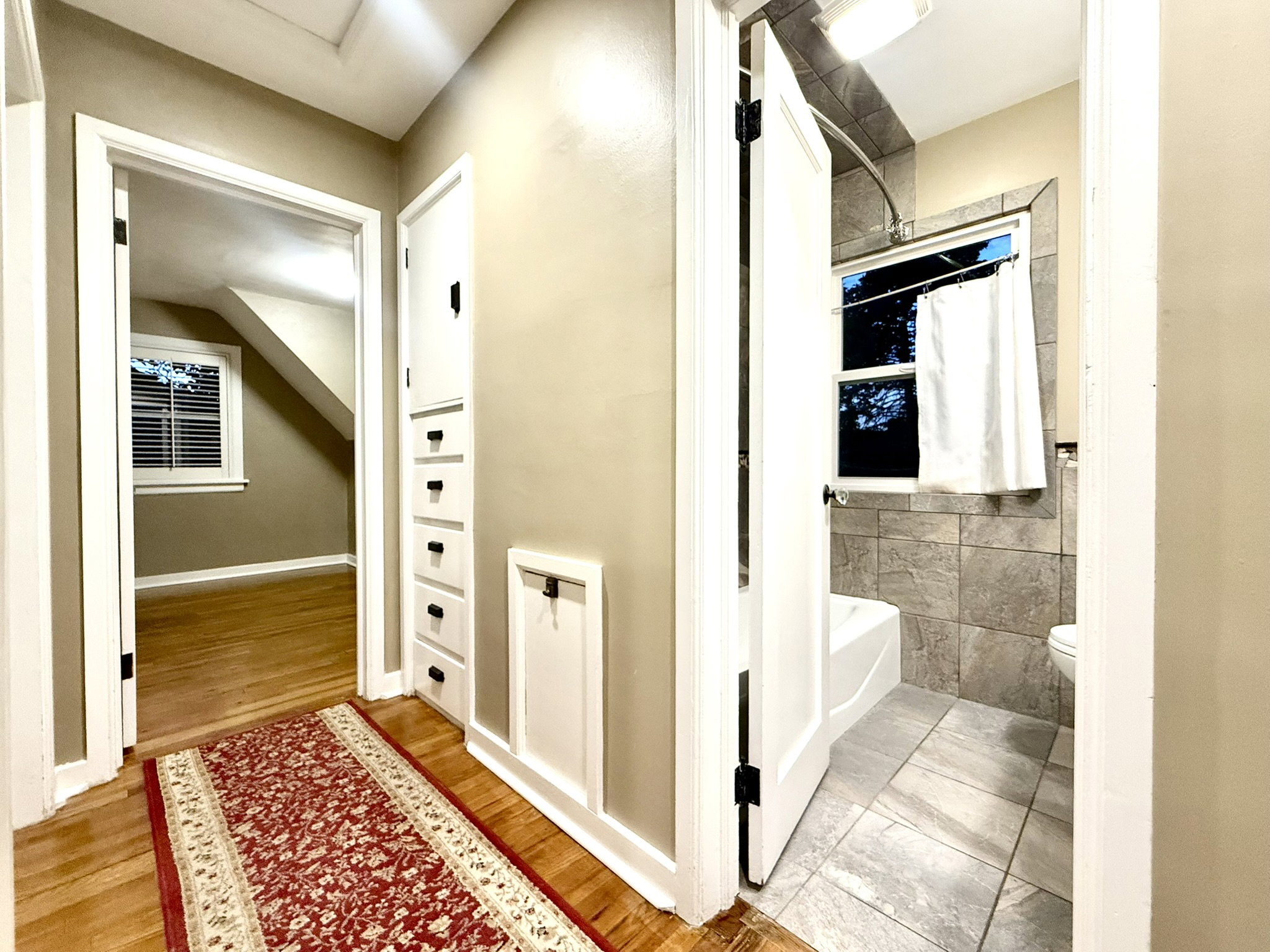 Hallway with Built in cabinets Well-appointed bathroom featuring a white bathtub, tiled shower surround, and tiled flooring