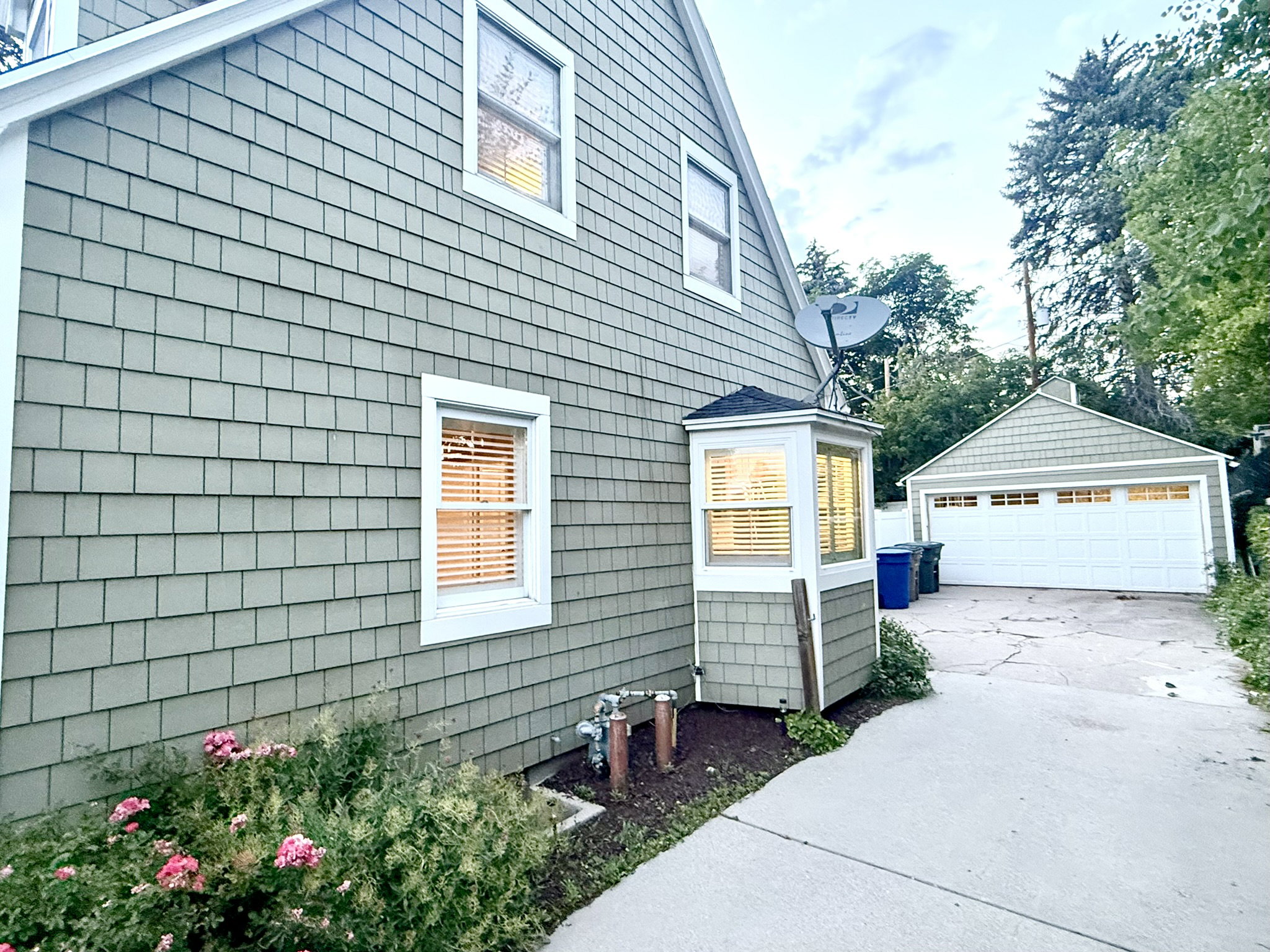 Shingle-sided exterior featuring a bay window, white-trimmed windows, and a detached two-car garage with a white panel door