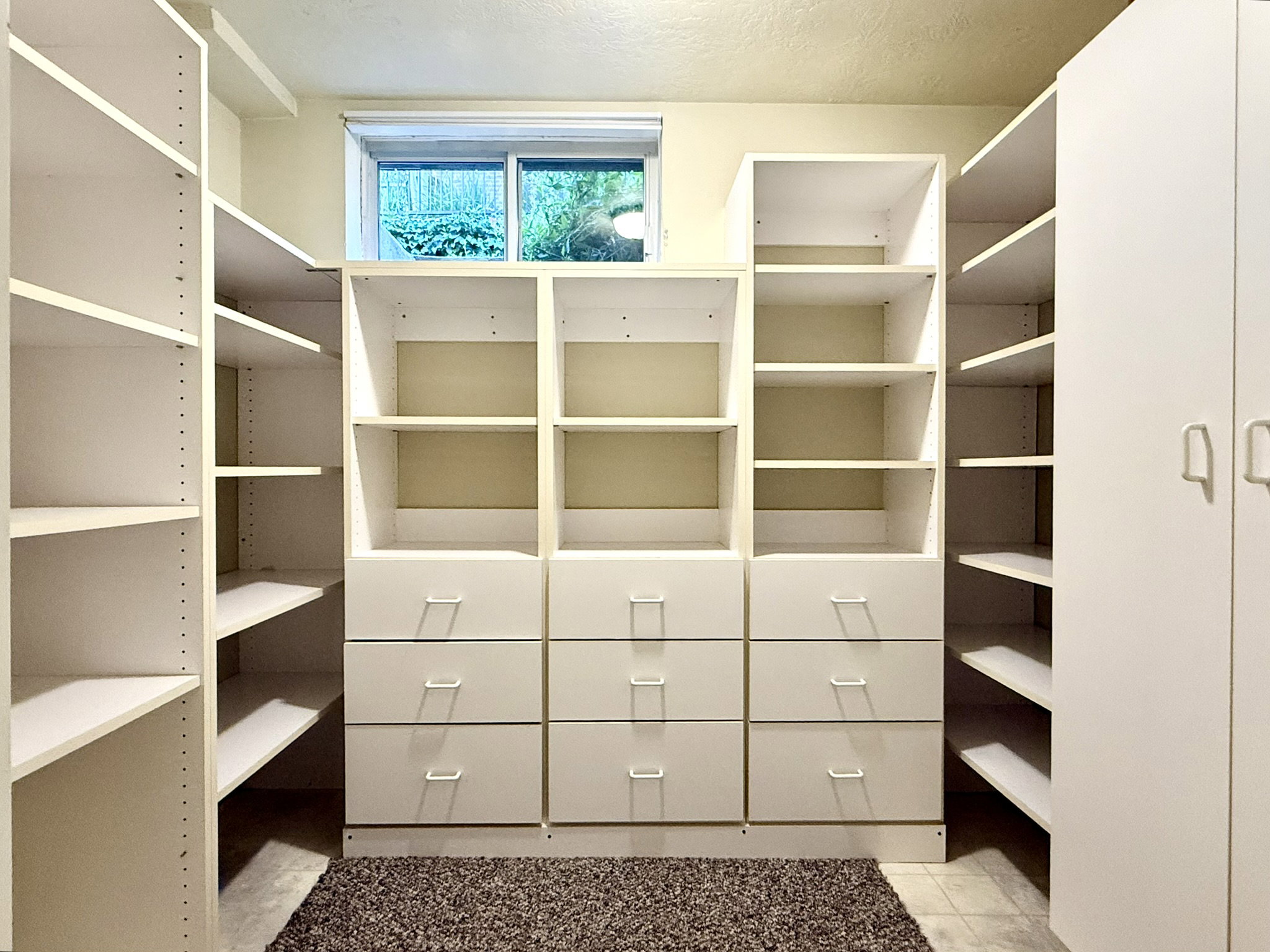 Storage Room Custom white built-in shelving with adjustable shelves, integrated drawers, and a window providing natural light
