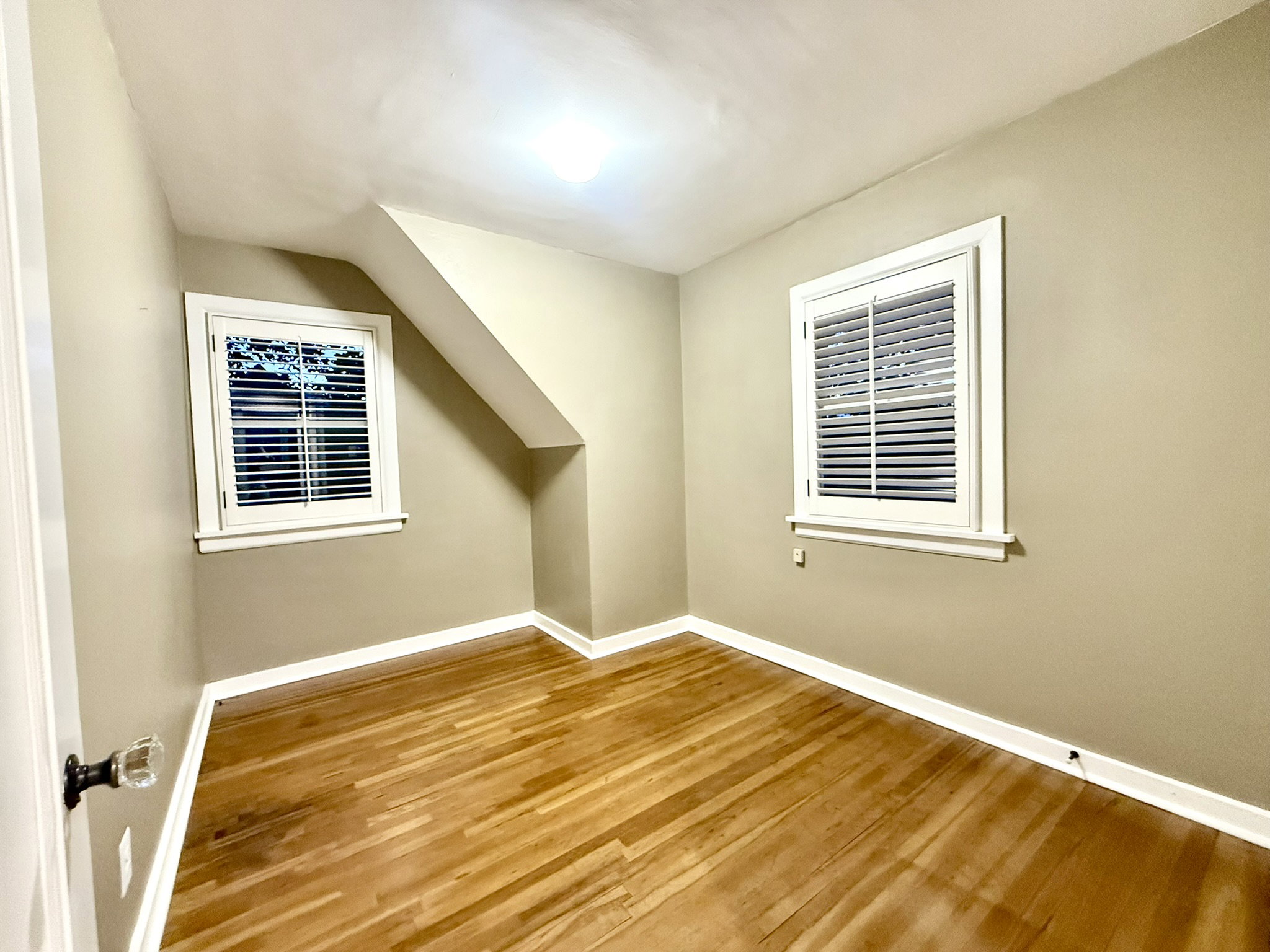 Bedroom #3  featuring wood-finish flooring, two windows with white louvered shutters, and an angled ceiling detail